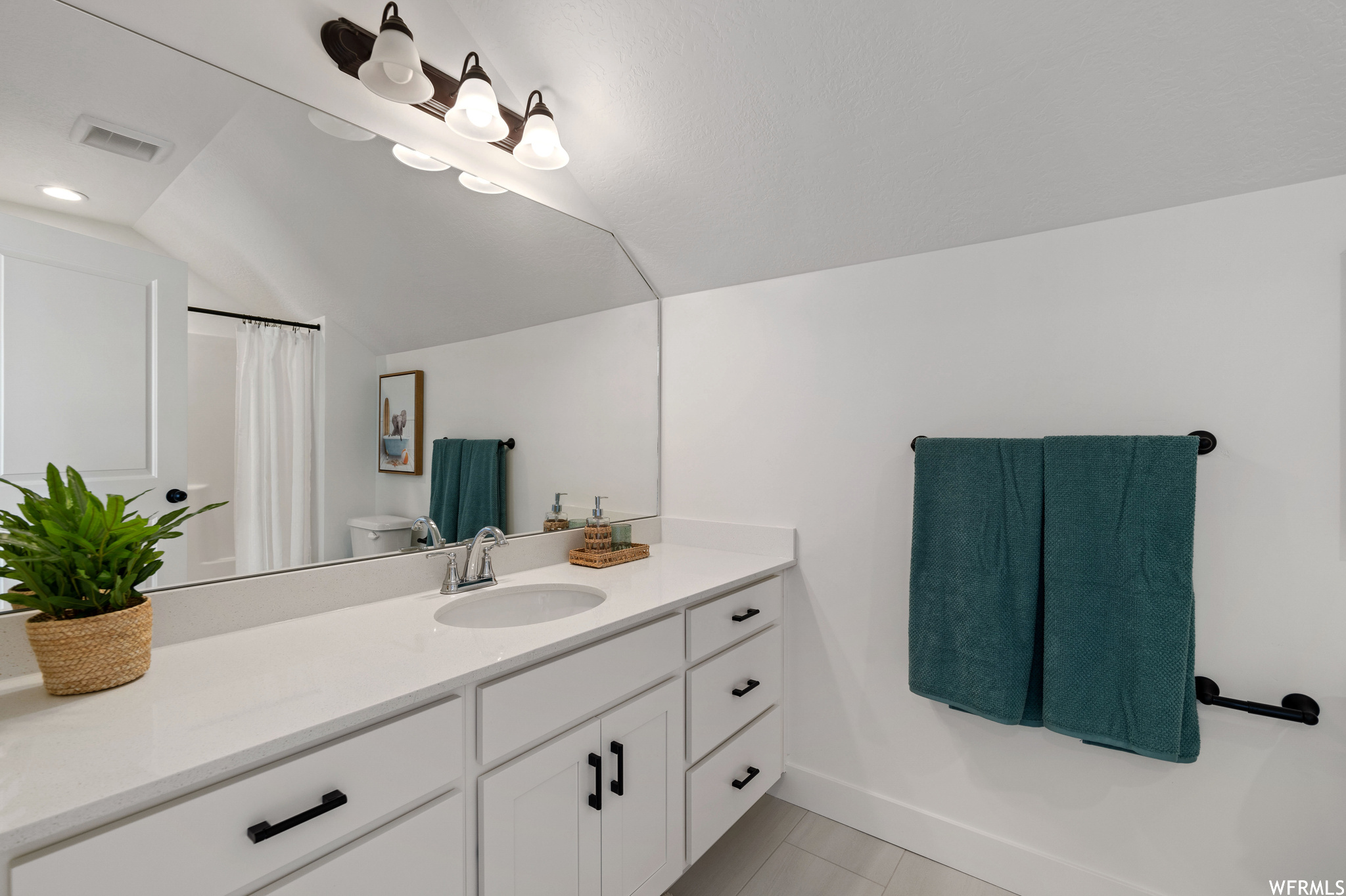 Bathroom featuring lofted ceiling, oversized vanity, toilet, and tile flooring