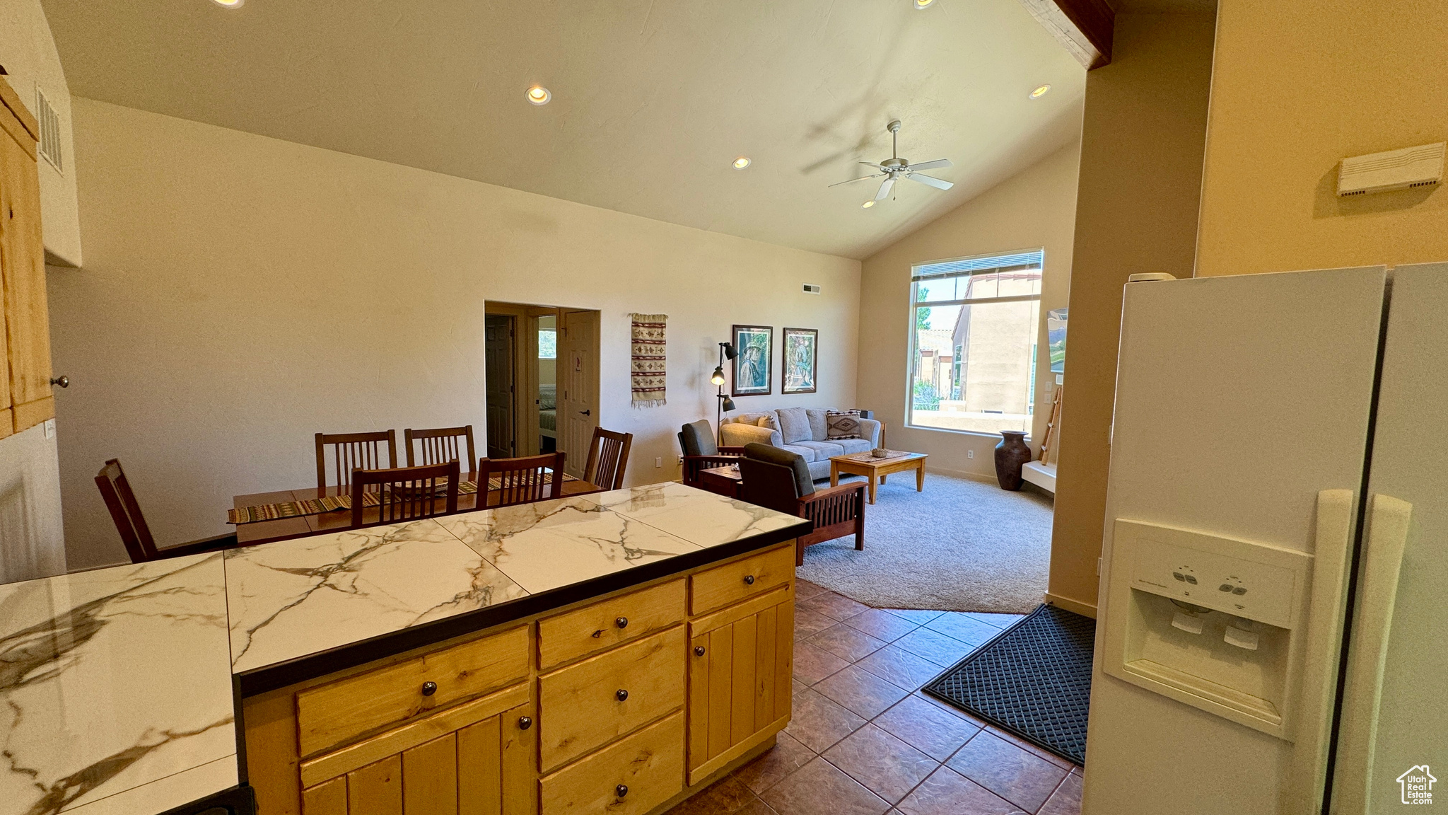 Kitchen featuring light tile patterned floors, light stone counters, ceiling fan, white refrigerator with ice dispenser, and high vaulted ceiling