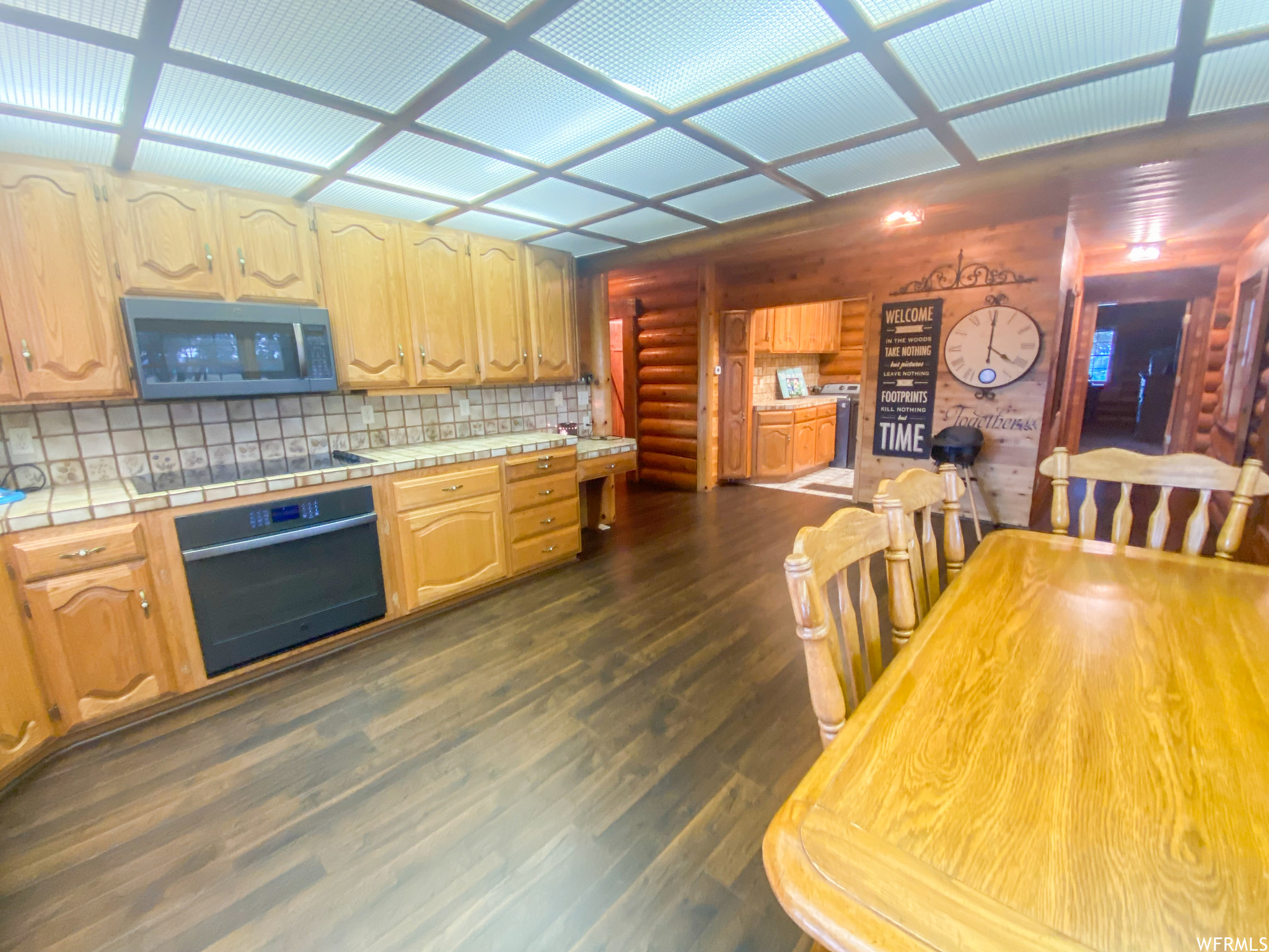 Kitchen with black appliances, dark hardwood / wood-style flooring, tile countertops, and backsplash