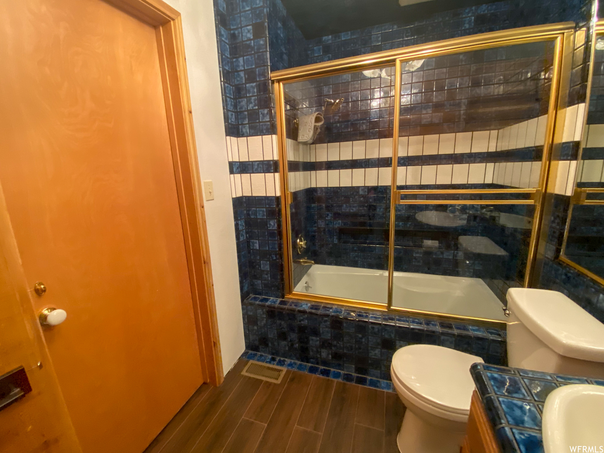 Full bathroom featuring hardwood / wood-style floors, shower / bath combination with glass door, sink, and toilet