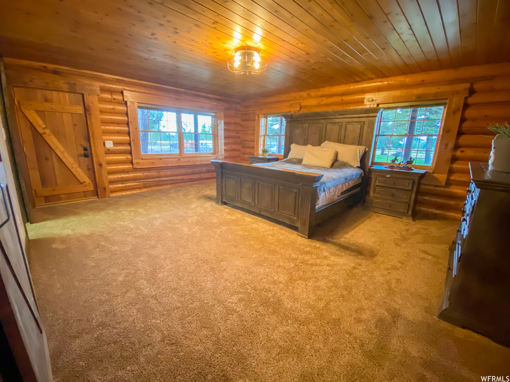 Carpeted bedroom with rustic walls, multiple windows, and wood ceiling