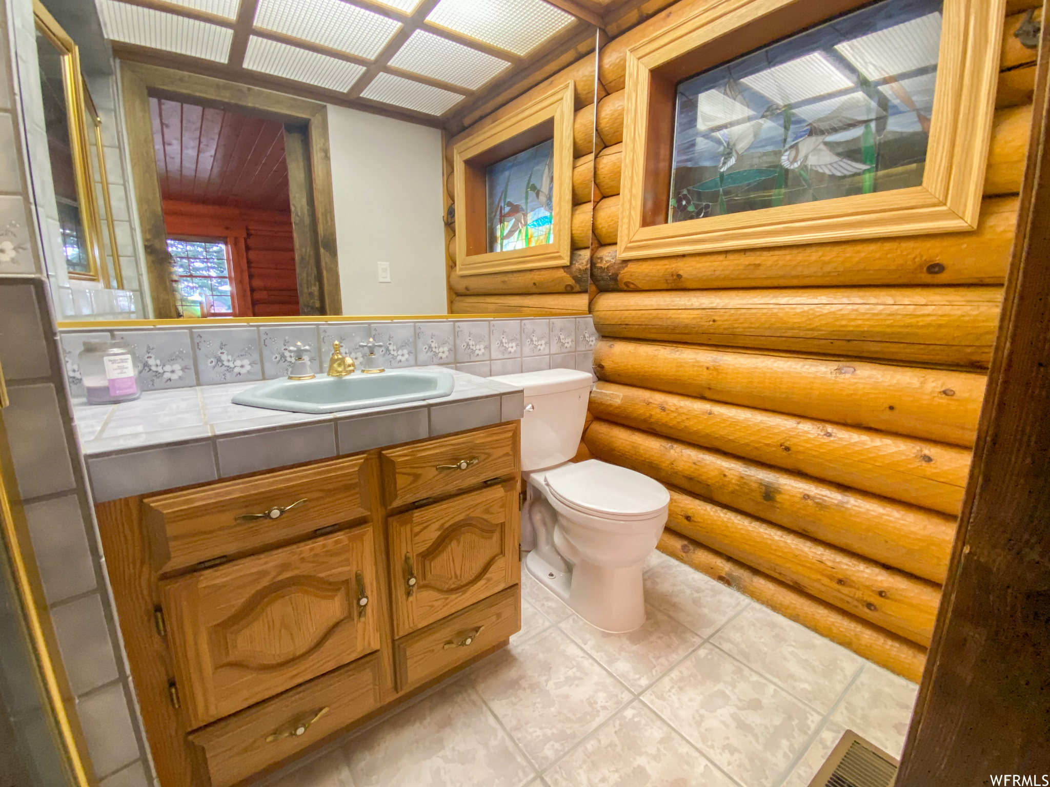 Bathroom featuring log walls, large vanity, toilet, backsplash, and tile flooring