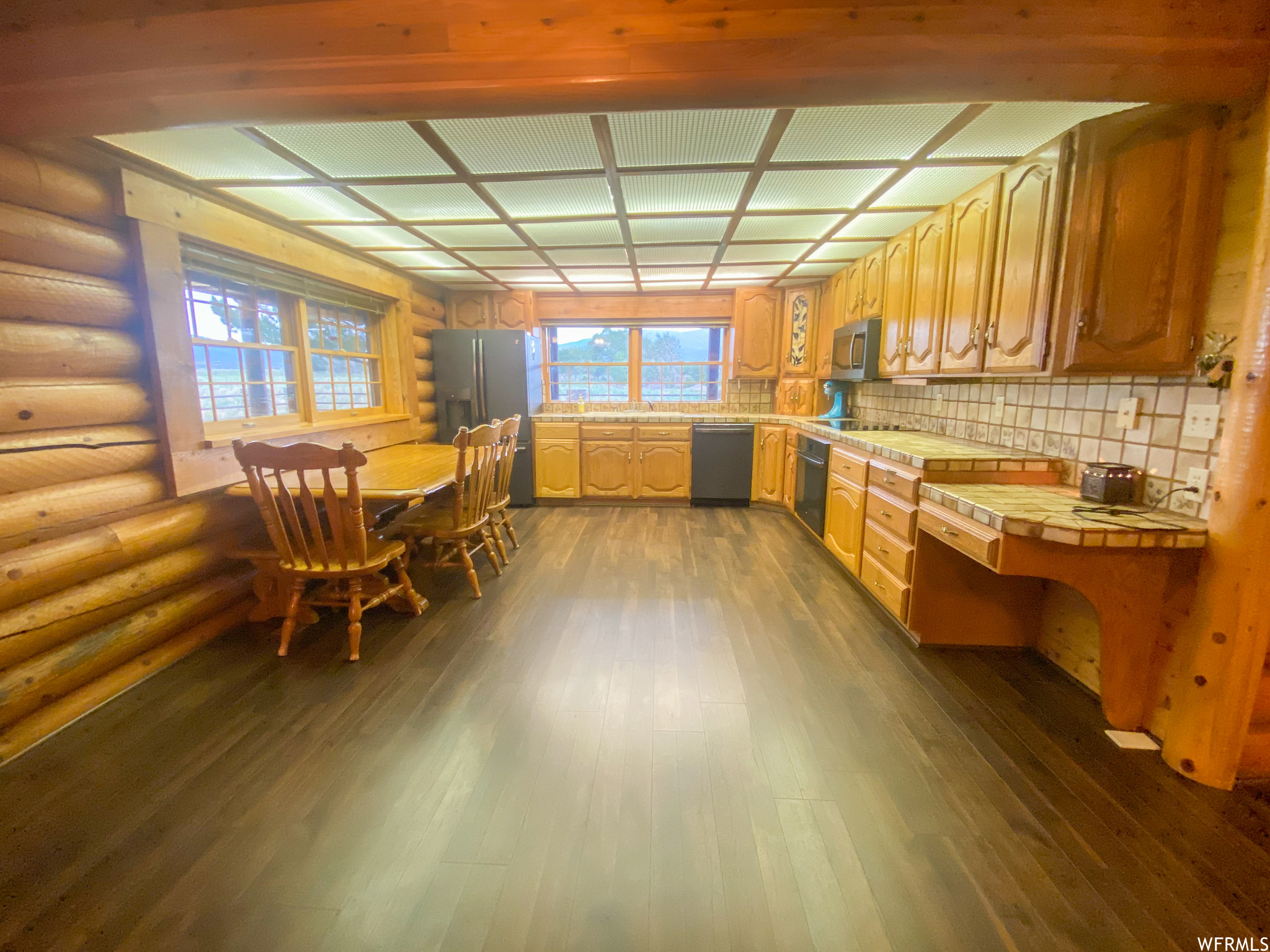 Kitchen with tile countertops, stainless steel appliances, rustic walls, tasteful backsplash, and dark wood-type flooring