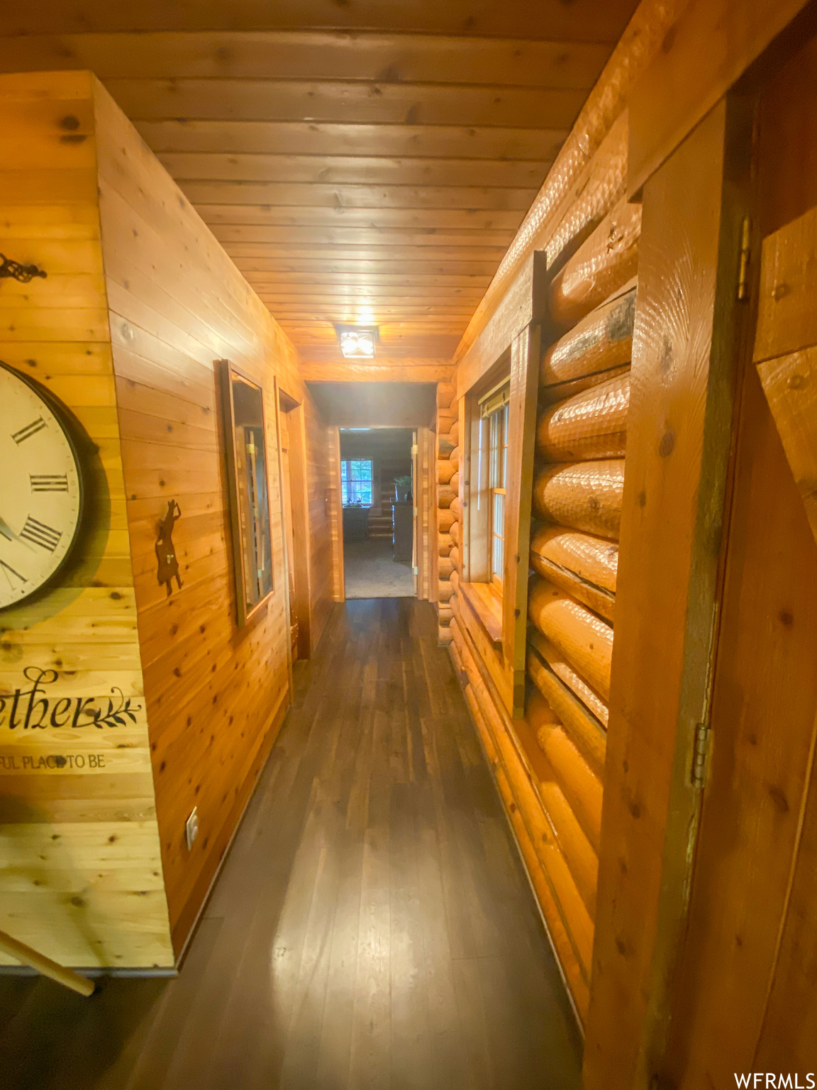 Hallway featuring dark wood-type flooring, wooden walls, log walls, and wood ceiling