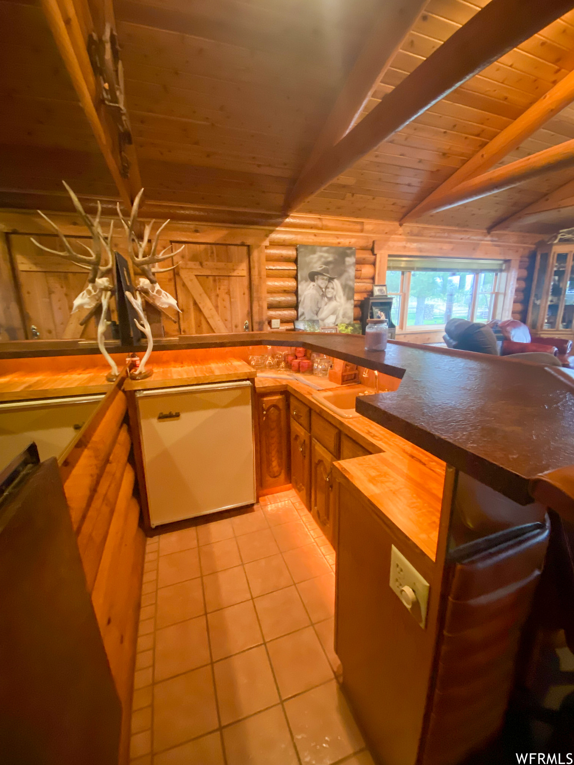 Kitchen featuring light tile floors, wood ceiling, kitchen peninsula, vaulted ceiling with beams, and dishwashing machine