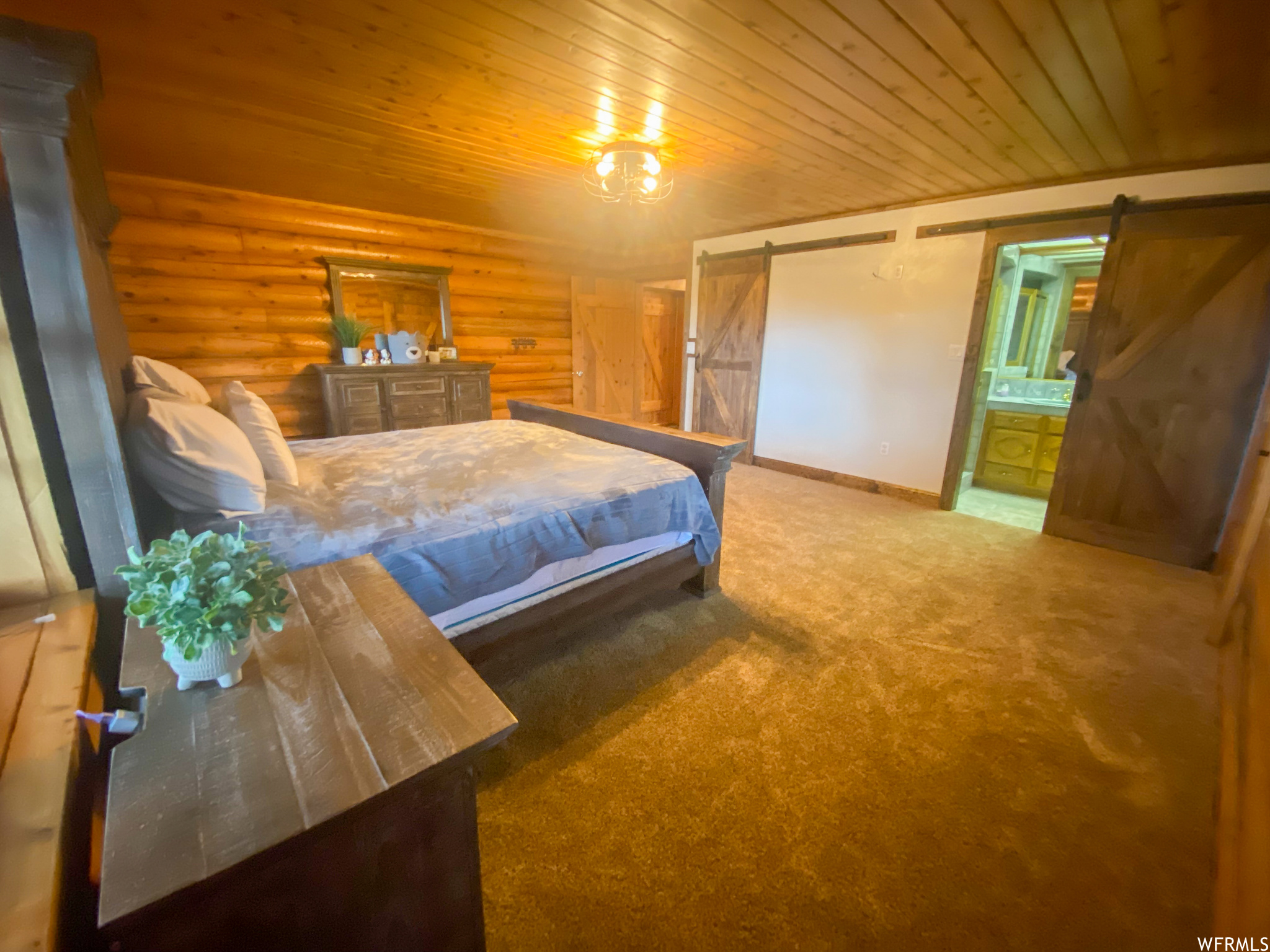 Carpeted bedroom featuring log walls, a barn door, connected bathroom, and wooden ceiling