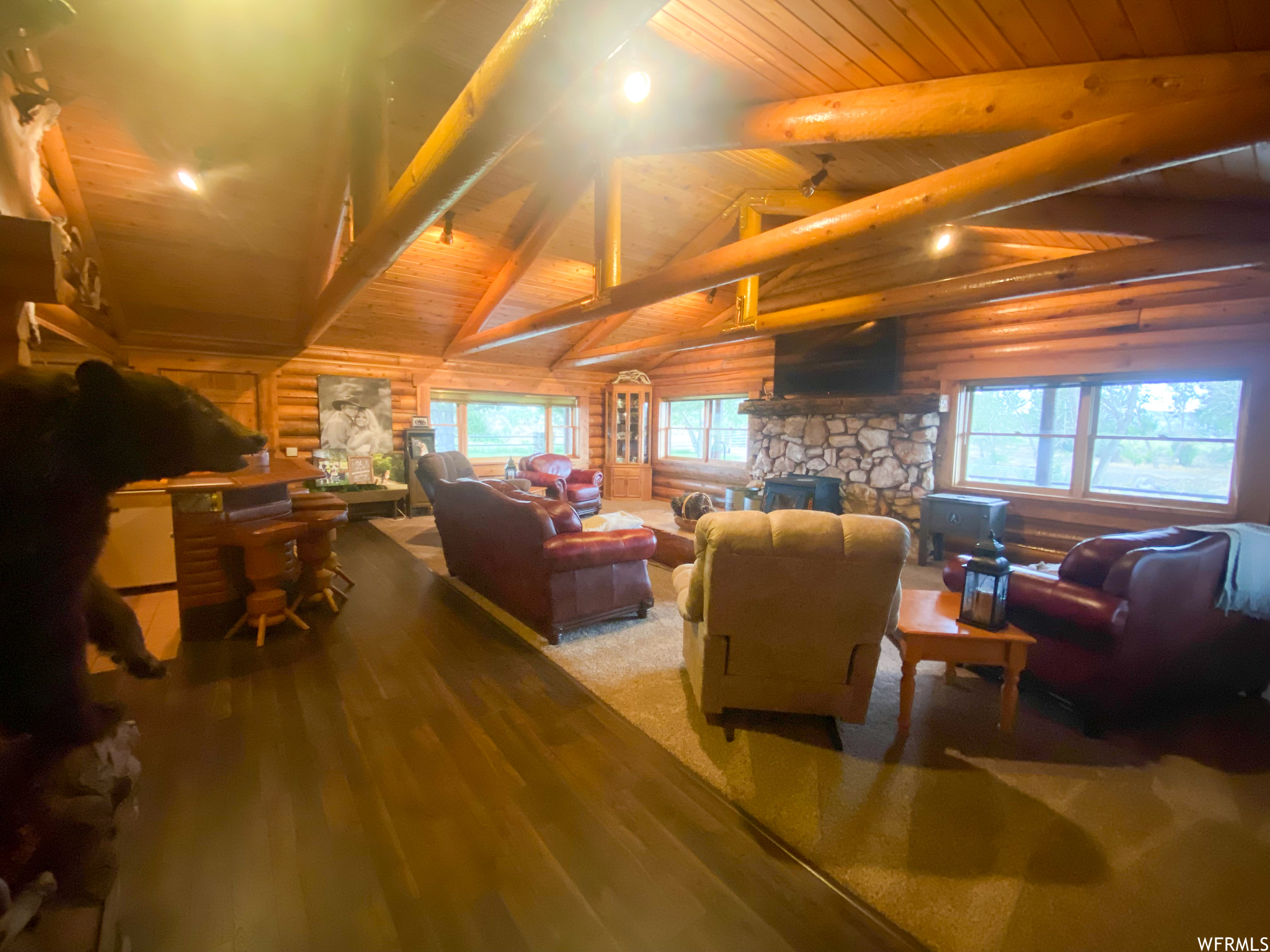 Living room with vaulted ceiling with beams, log walls, a fireplace, and wood ceiling