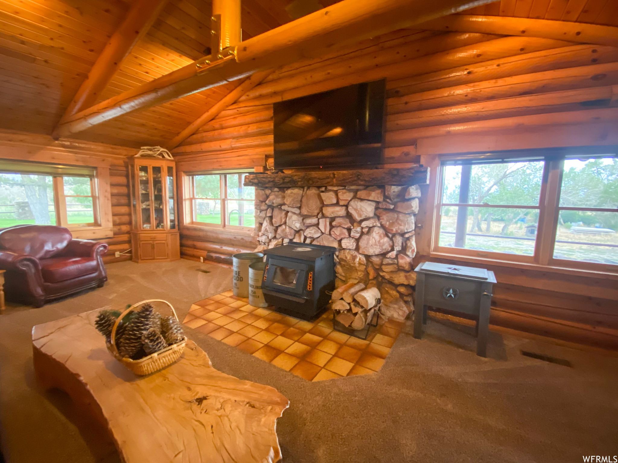 Unfurnished living room with wooden ceiling, log walls, carpet, a wood stove, and beam ceiling