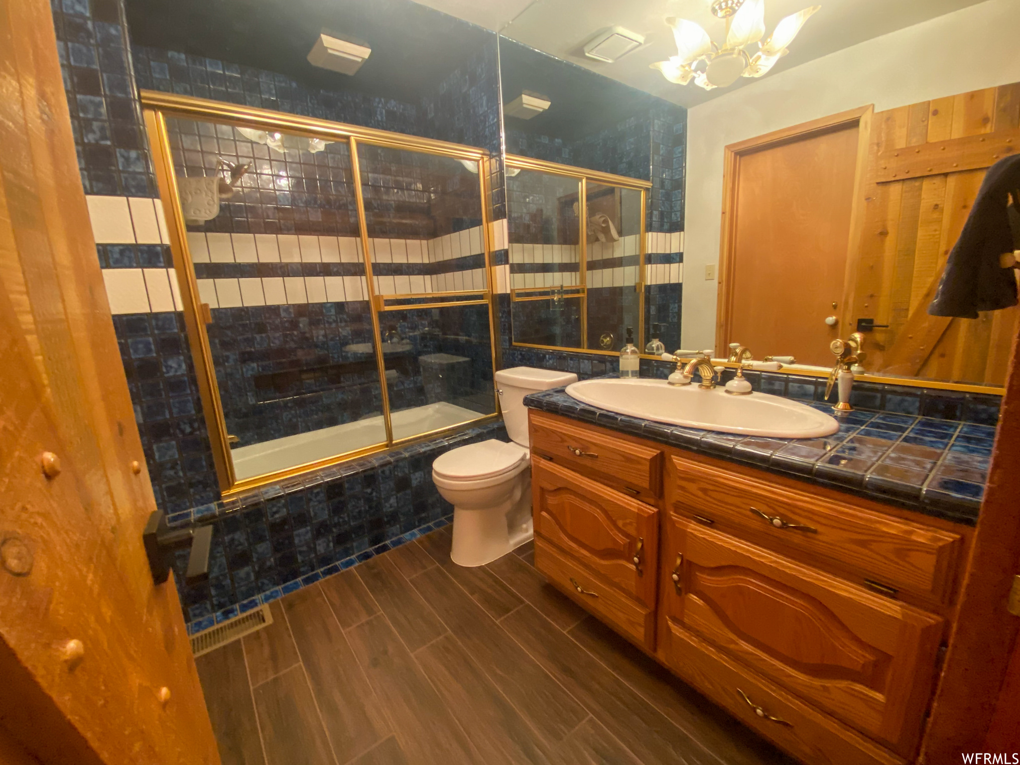 Full bathroom with vanity, a chandelier, toilet, combined bath / shower with glass door, and wood walls