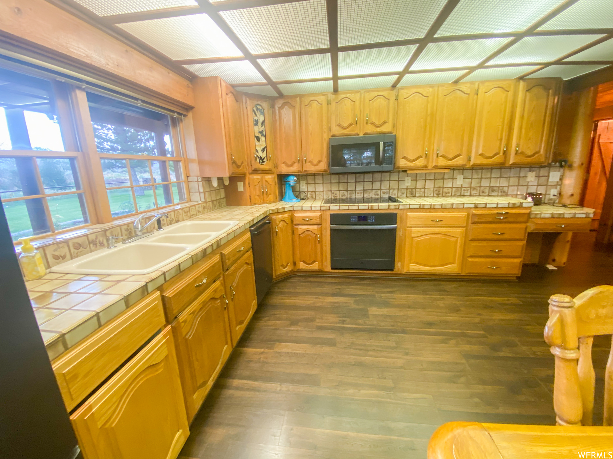 Kitchen with black appliances, tile countertops, dark wood-type flooring, and backsplash