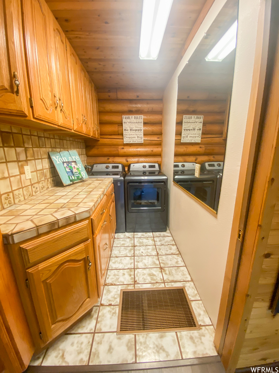 Kitchen with log walls, light tile floors, tile counters, washer and clothes dryer, and backsplash