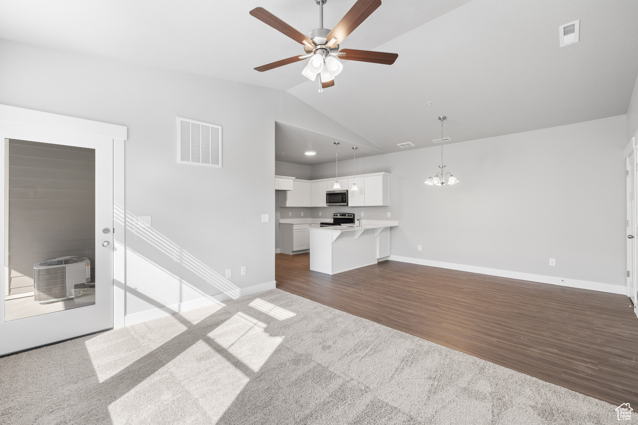 Unfurnished living room featuring carpet flooring, vaulted ceiling, and ceiling fan with notable chandelier