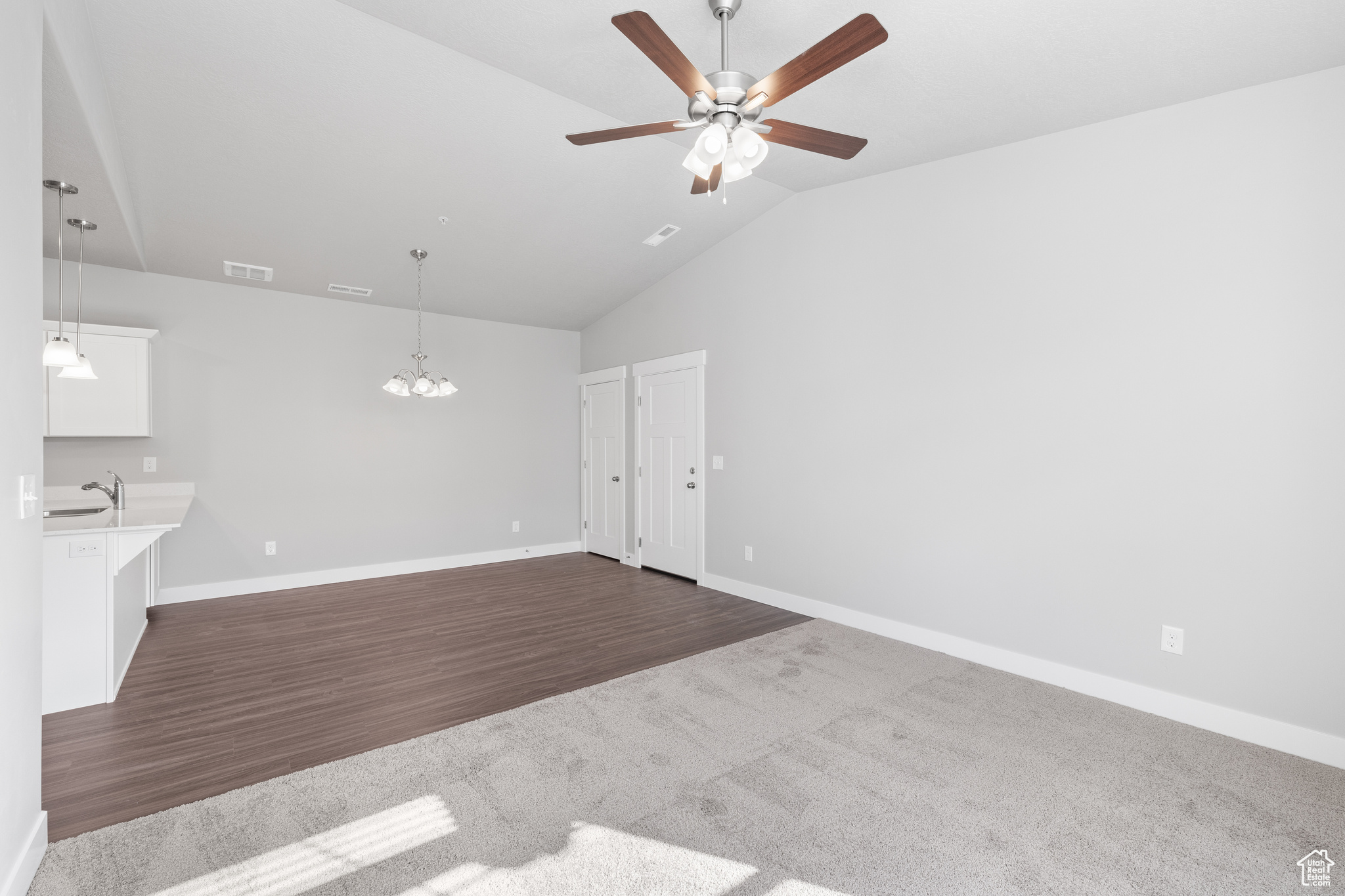 Unfurnished living room featuring vaulted ceiling, sink, dark colored carpet, and ceiling fan with notable chandelier