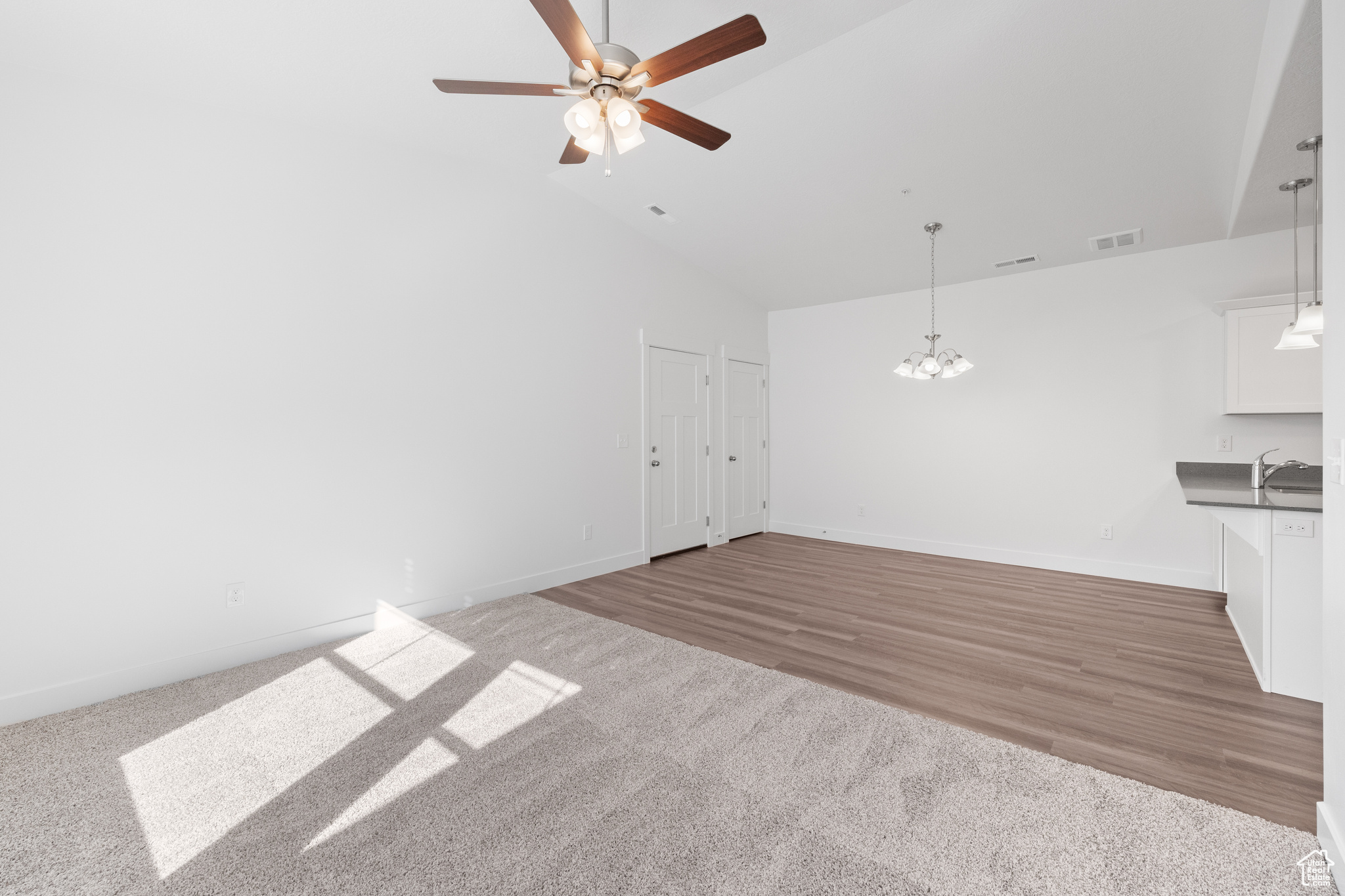 Unfurnished living room with high vaulted ceiling, carpet floors, and ceiling fan with notable chandelier