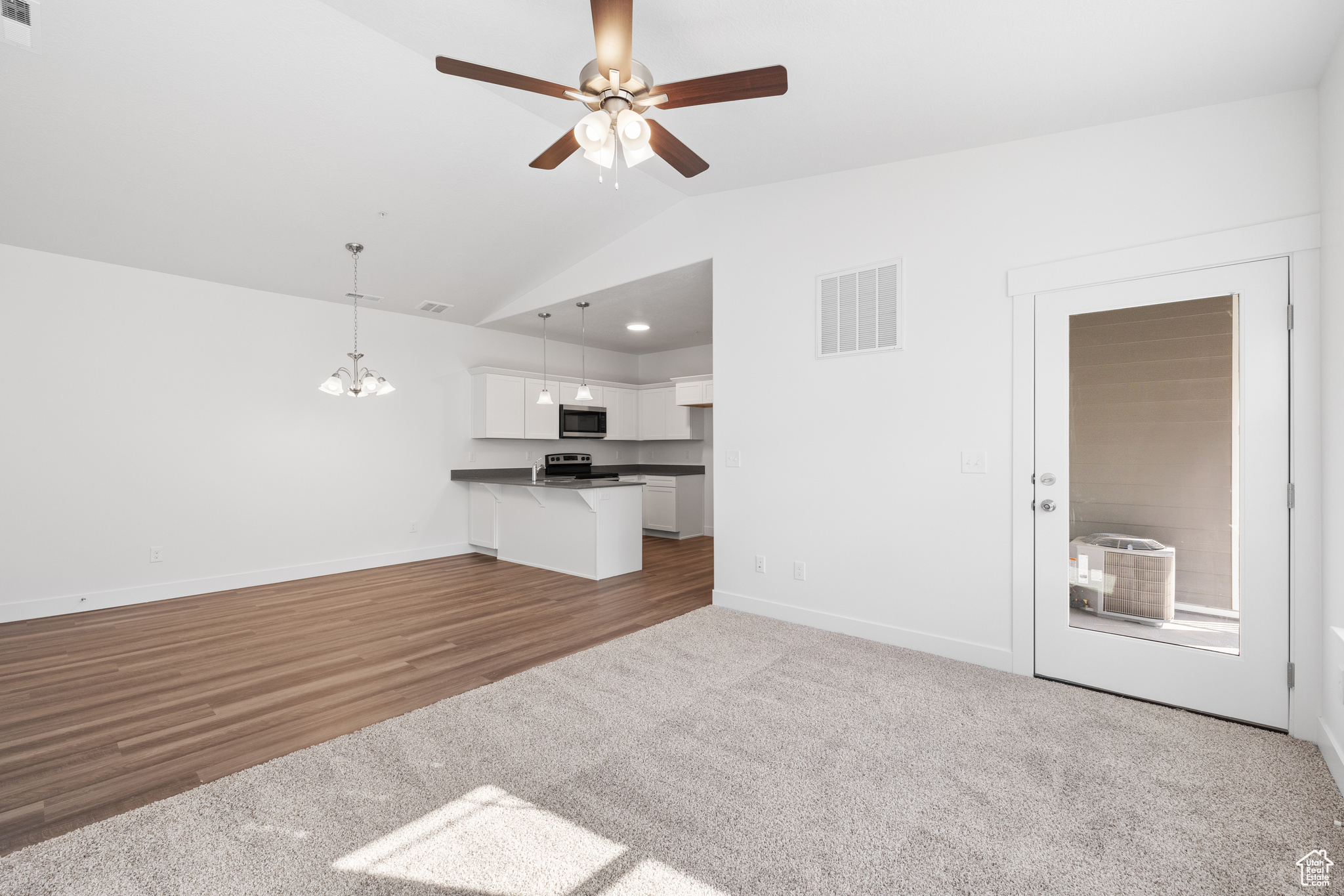 Unfurnished living room featuring light colored carpet, ceiling fan with notable chandelier, and lofted ceiling