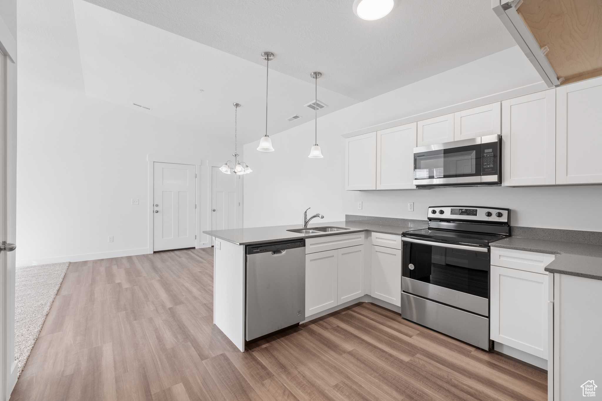 Kitchen with light hardwood / wood-style floors, kitchen peninsula, white cabinetry, appliances with stainless steel finishes, and sink