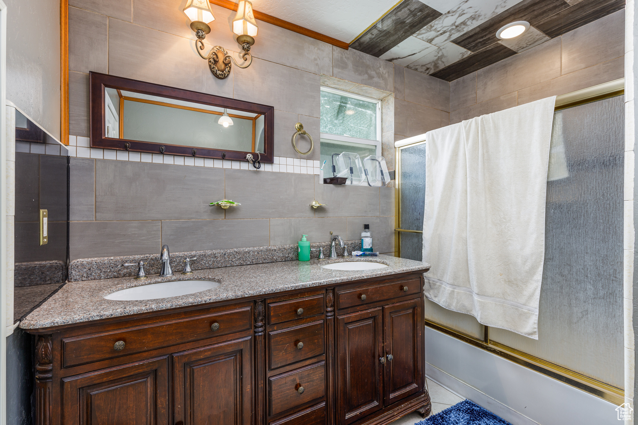 Bathroom with double vanity, tile walls, and enclosed tub / shower combo