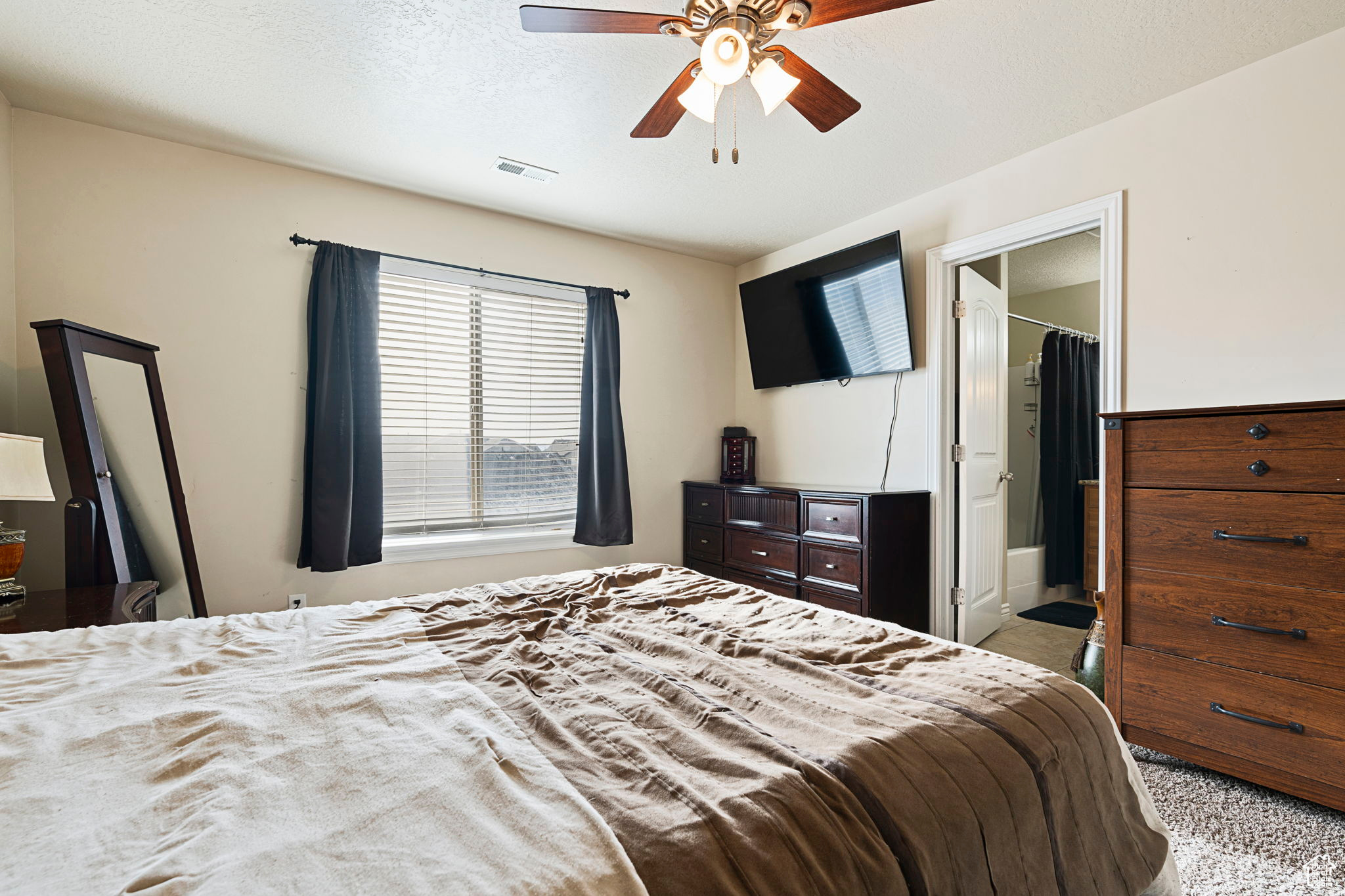 Bedroom with ceiling fan, a spacious closet, ensuite bath, light colored carpet, and a closet