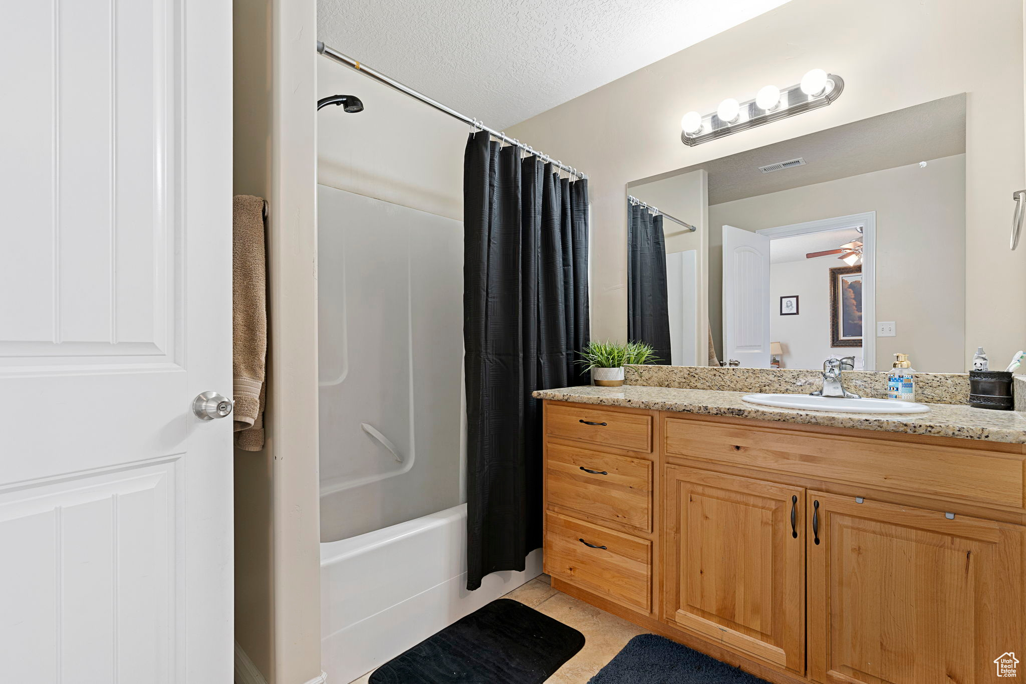 Bathroom with vanity, a textured ceiling, tile floors, ceiling fan, and shower / tub combo