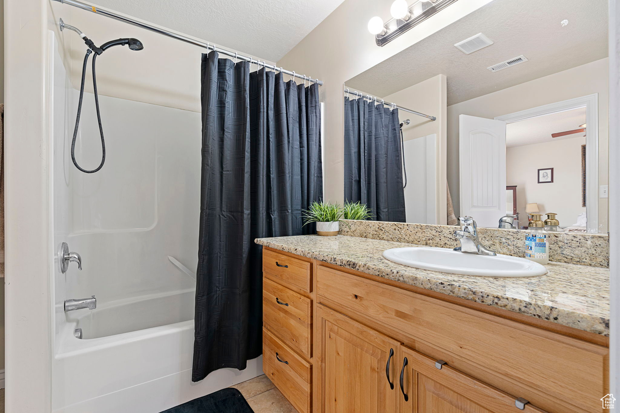Bathroom featuring tile floors, large vanity, a textured ceiling, and shower / bathtub combination with curtain