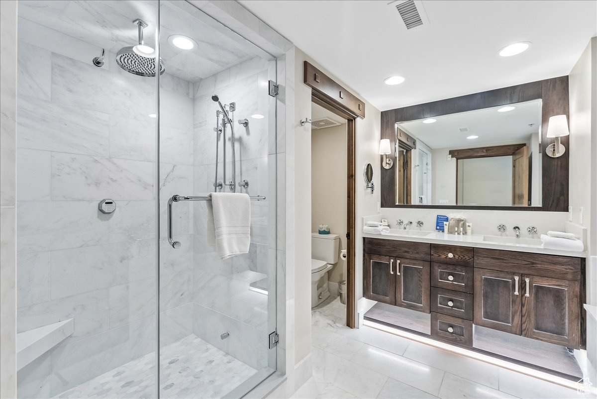 Bathroom with a shower with shower door, tile floors, toilet, and double sink vanity