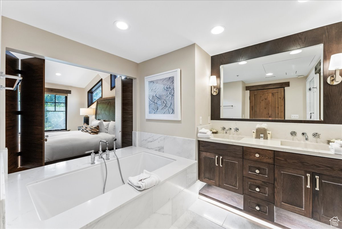 Bathroom featuring a relaxing tiled bath, dual sinks, vanity with extensive cabinet space, tile flooring, and backsplash
