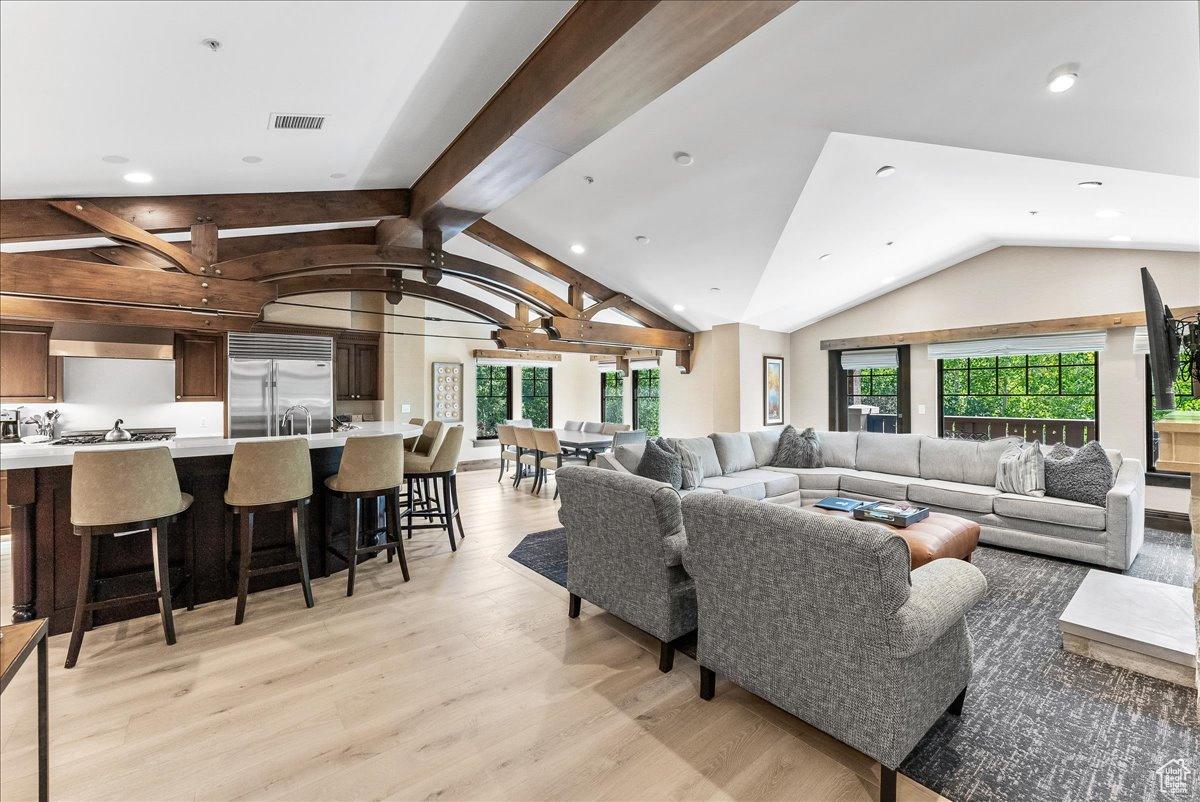 Living room featuring light hardwood / wood-style flooring, vaulted ceiling with beams, and plenty of natural light
