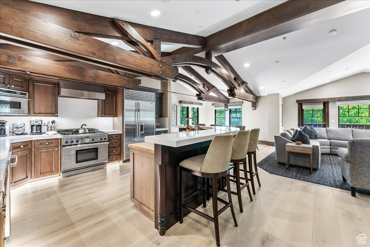 Kitchen with a kitchen island, lofted ceiling with beams, wall chimney exhaust hood, light hardwood / wood-style flooring, and high quality appliances