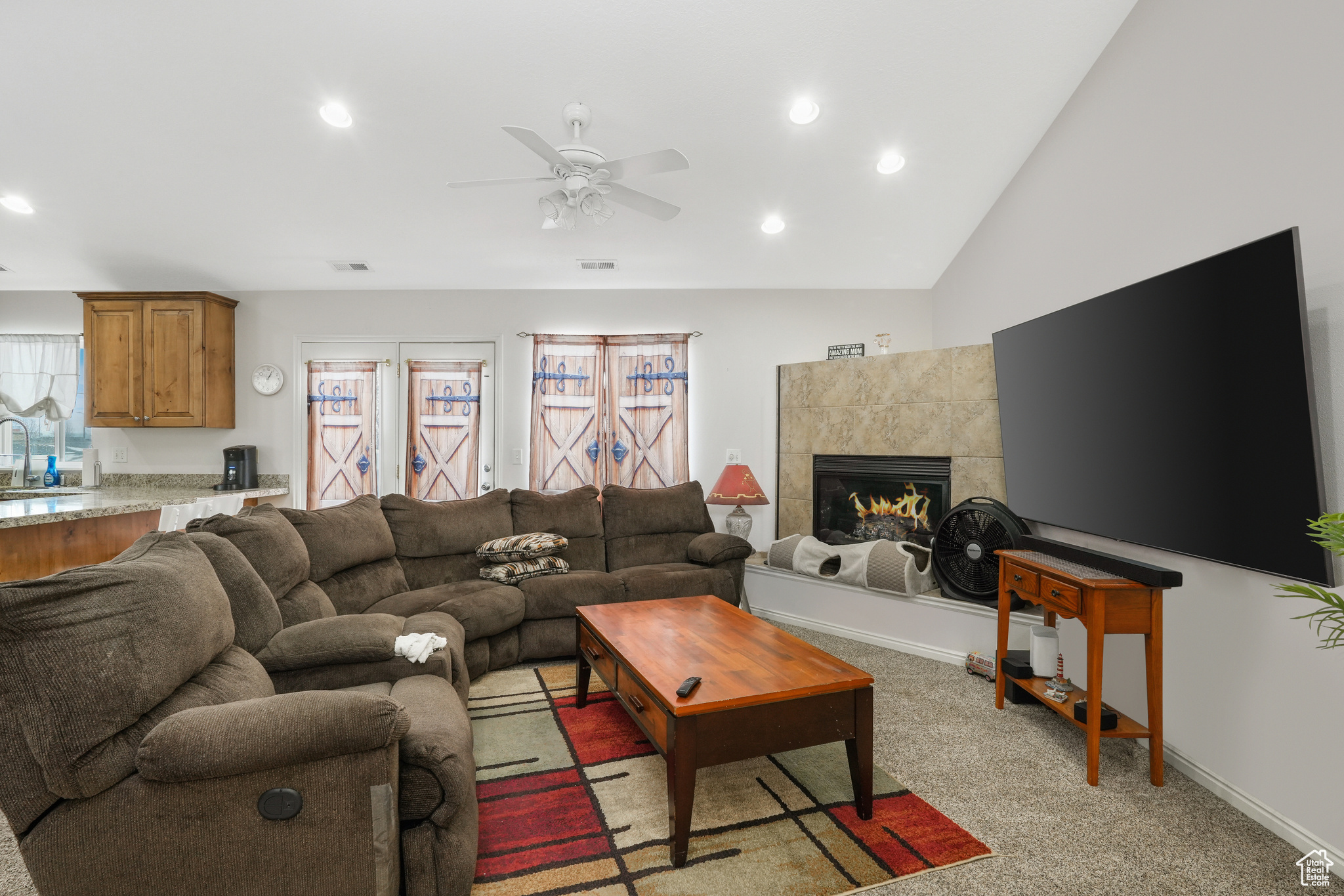Living room featuring a tile fireplace, light carpet, ceiling fan, sink, and vaulted ceiling