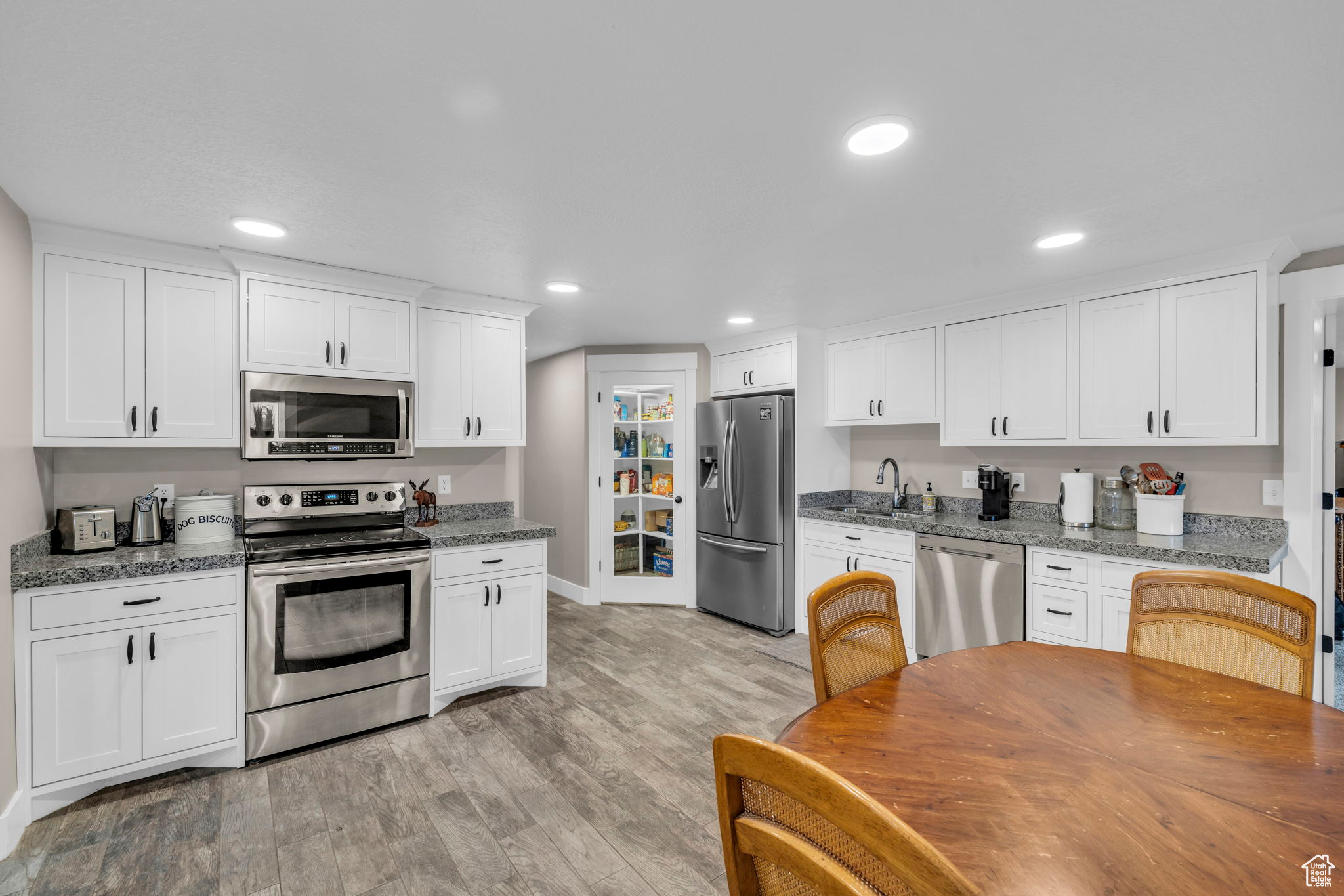 Kitchen featuring light wood-type flooring, appliances with stainless steel finishes, light stone counters, and white cabinetry