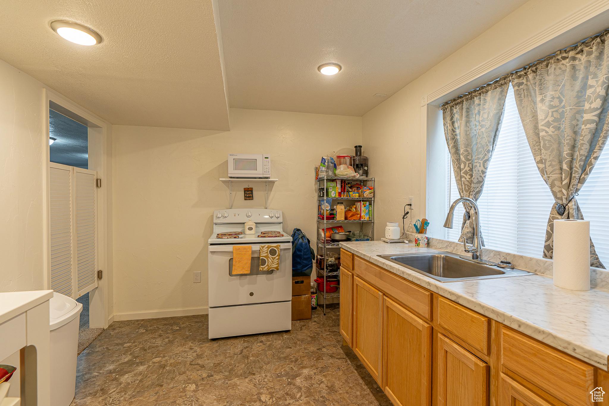 Kitchen with dark tile flooring, white appliances, and sink