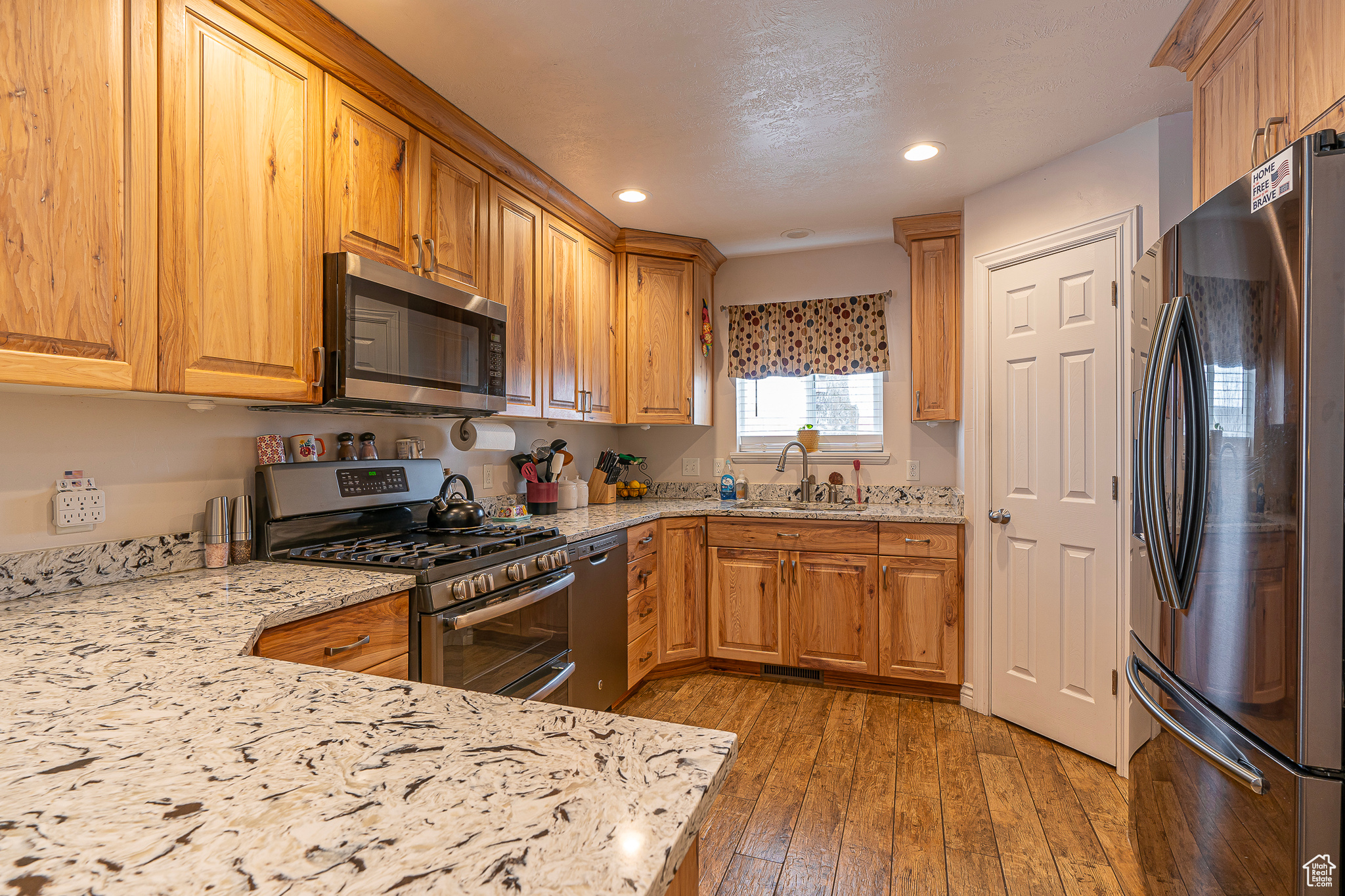 Kitchen with appliances with stainless steel finishes, light stone countertops, sink, and hardwood / wood-style floors