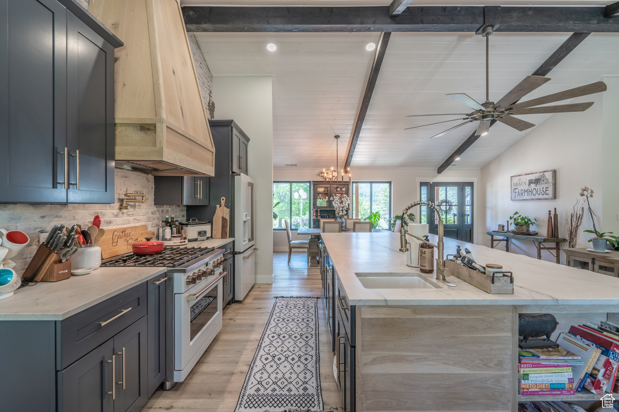 Kitchen with ceiling fan with notable chandelier, hanging light fixtures, lofted ceiling with beams, high end appliances, and a center island with sink