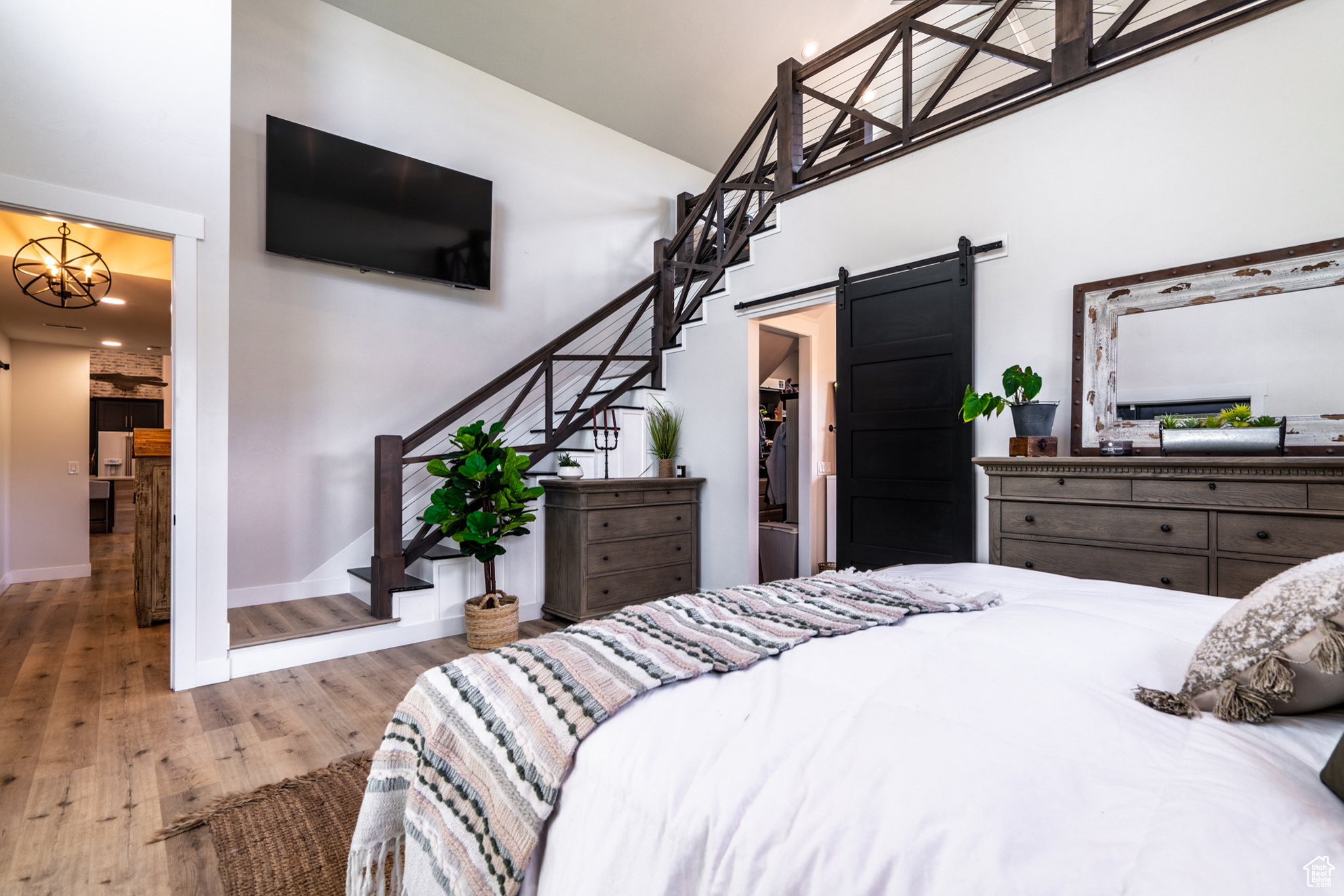 Bedroom featuring an inviting chandelier, a towering ceiling, a walk in closet, wood-type flooring, and a barn door