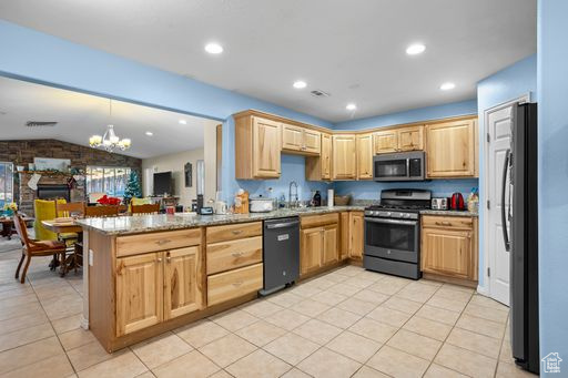 Kitchen with light tile flooring, appliances with stainless steel finishes, light stone counters, a notable chandelier, and kitchen peninsula