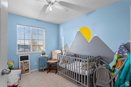 Bedroom featuring ceiling fan, a nursery area, and light carpet