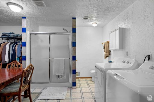 Clothes washing area featuring independent washer and dryer, a textured ceiling, and light tile floors
