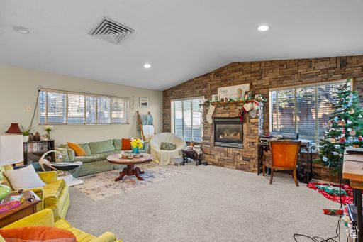 Carpeted living room featuring lofted ceiling and a stone fireplace