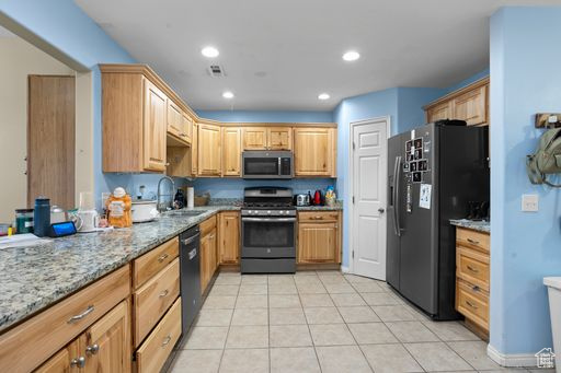 Kitchen featuring black appliances, sink, light tile flooring, and light stone countertops