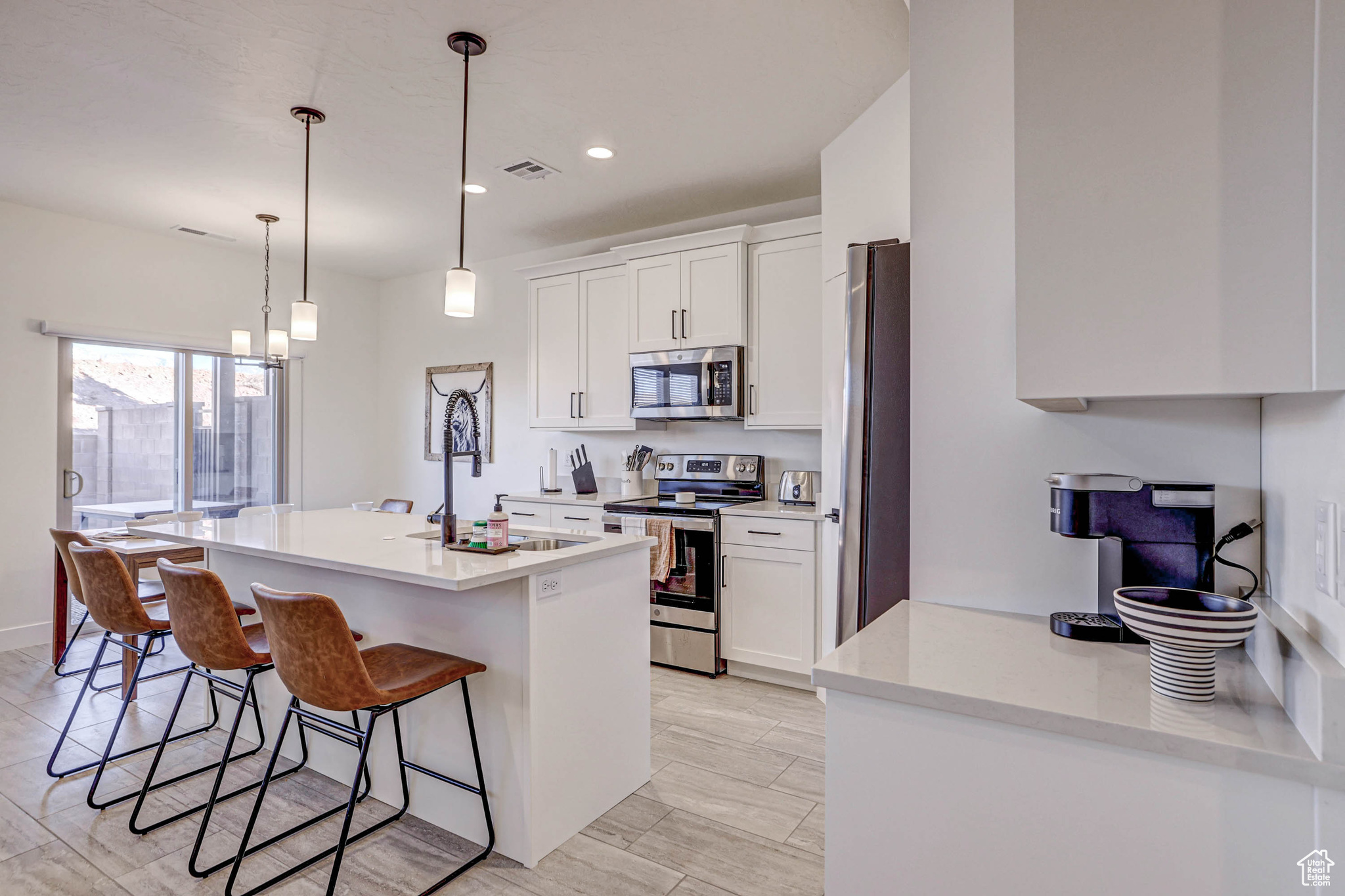 Kitchen featuring a breakfast bar, white cabinets, pendant lighting, stainless steel appliances, and an island with sink