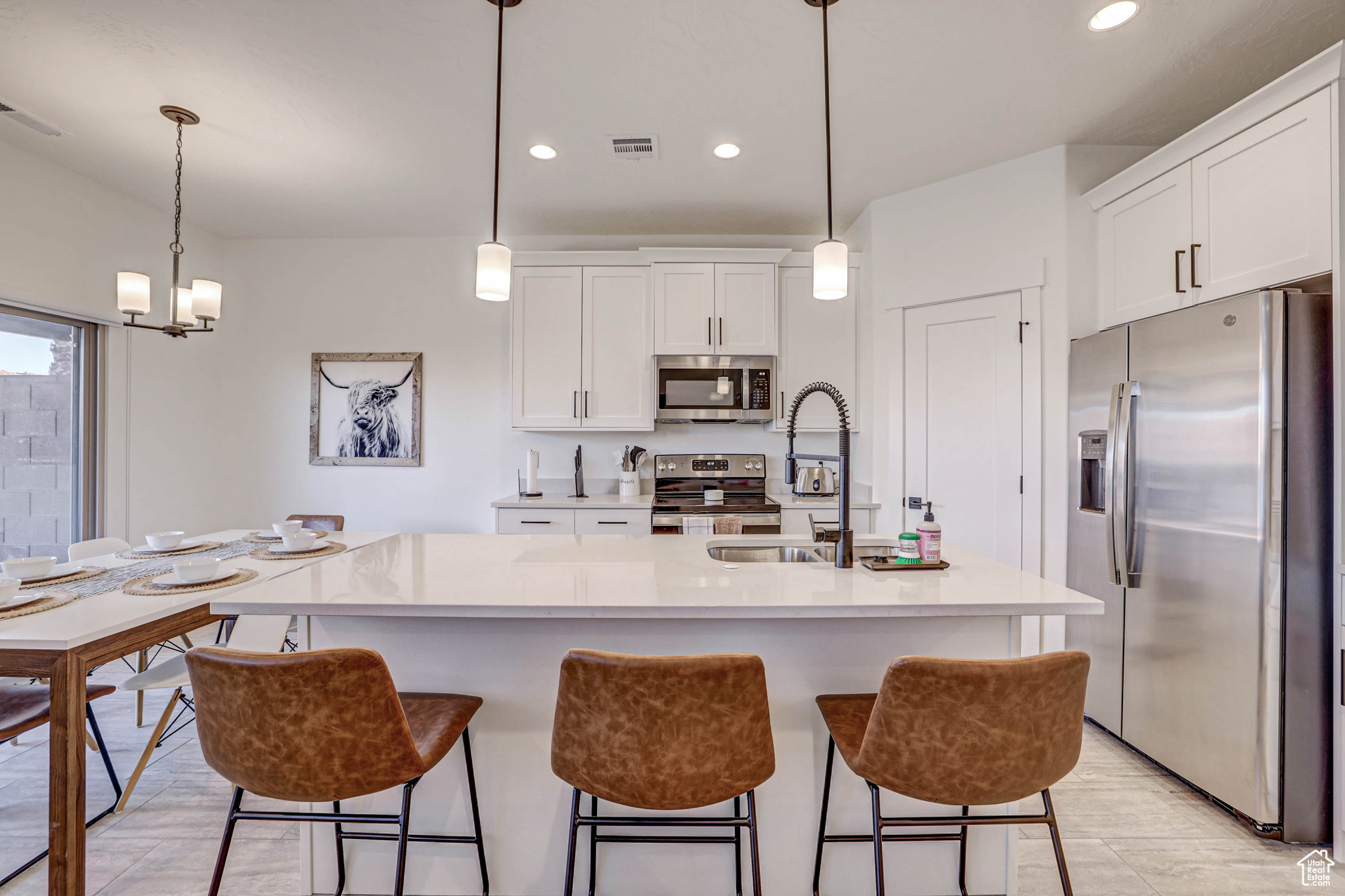 Kitchen with a breakfast bar area, white cabinets, decorative light fixtures, a center island with sink, and stainless steel appliances