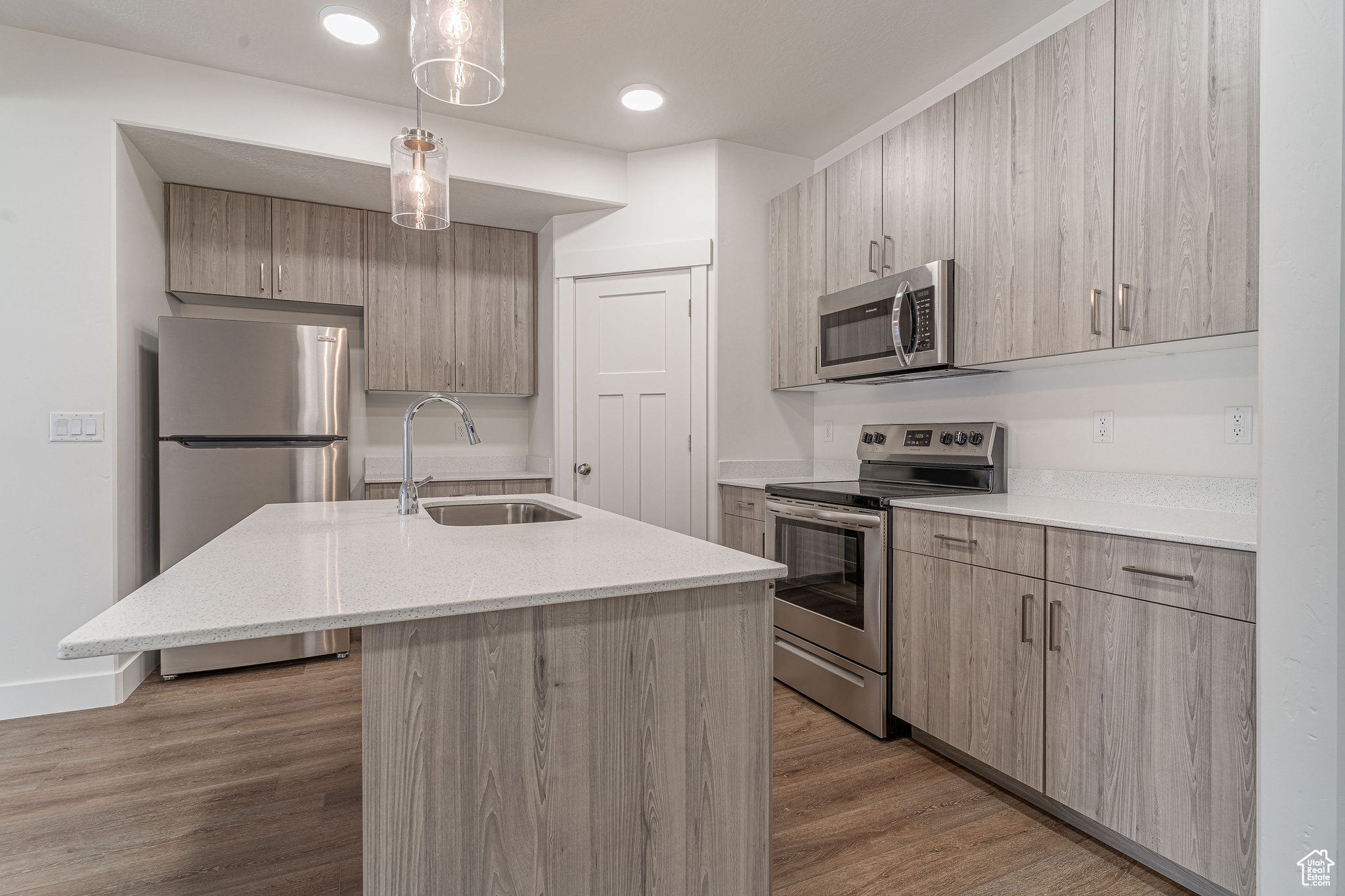 Kitchen featuring dark hardwood / wood-style flooring, decorative light fixtures, stainless steel appliances, sink, and a center island with sink
