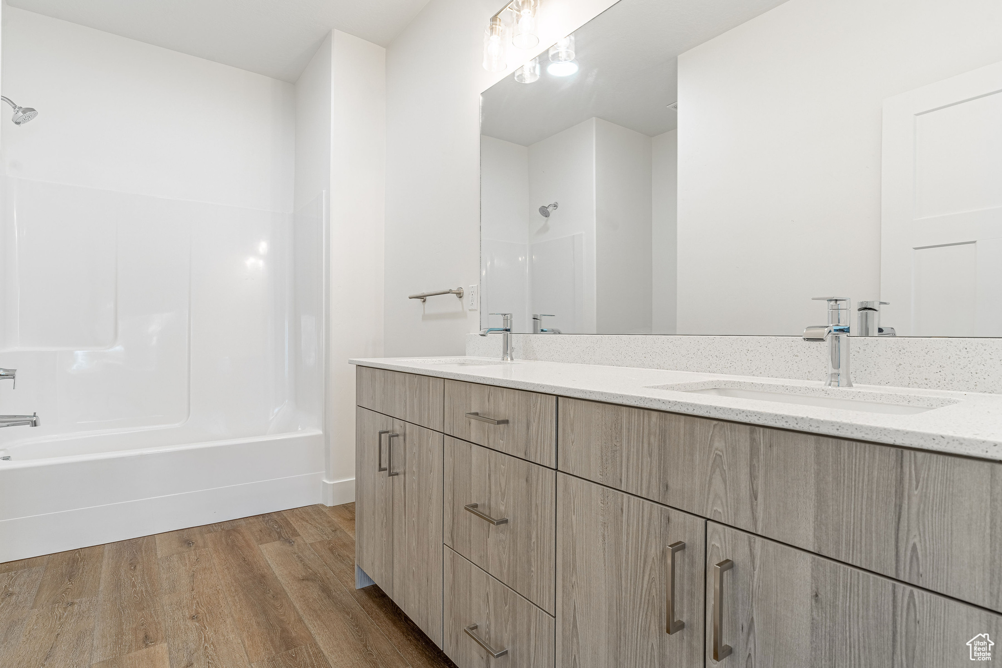 Bathroom with hardwood / wood-style floors, vanity with extensive cabinet space, shower / washtub combination, and double sink