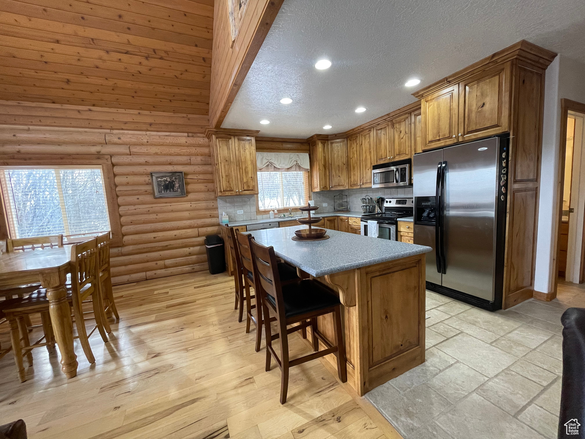 Kitchen featuring appliances with stainless steel finishes, a textured ceiling, light hardwood / wood-style flooring, rustic walls, and a kitchen island