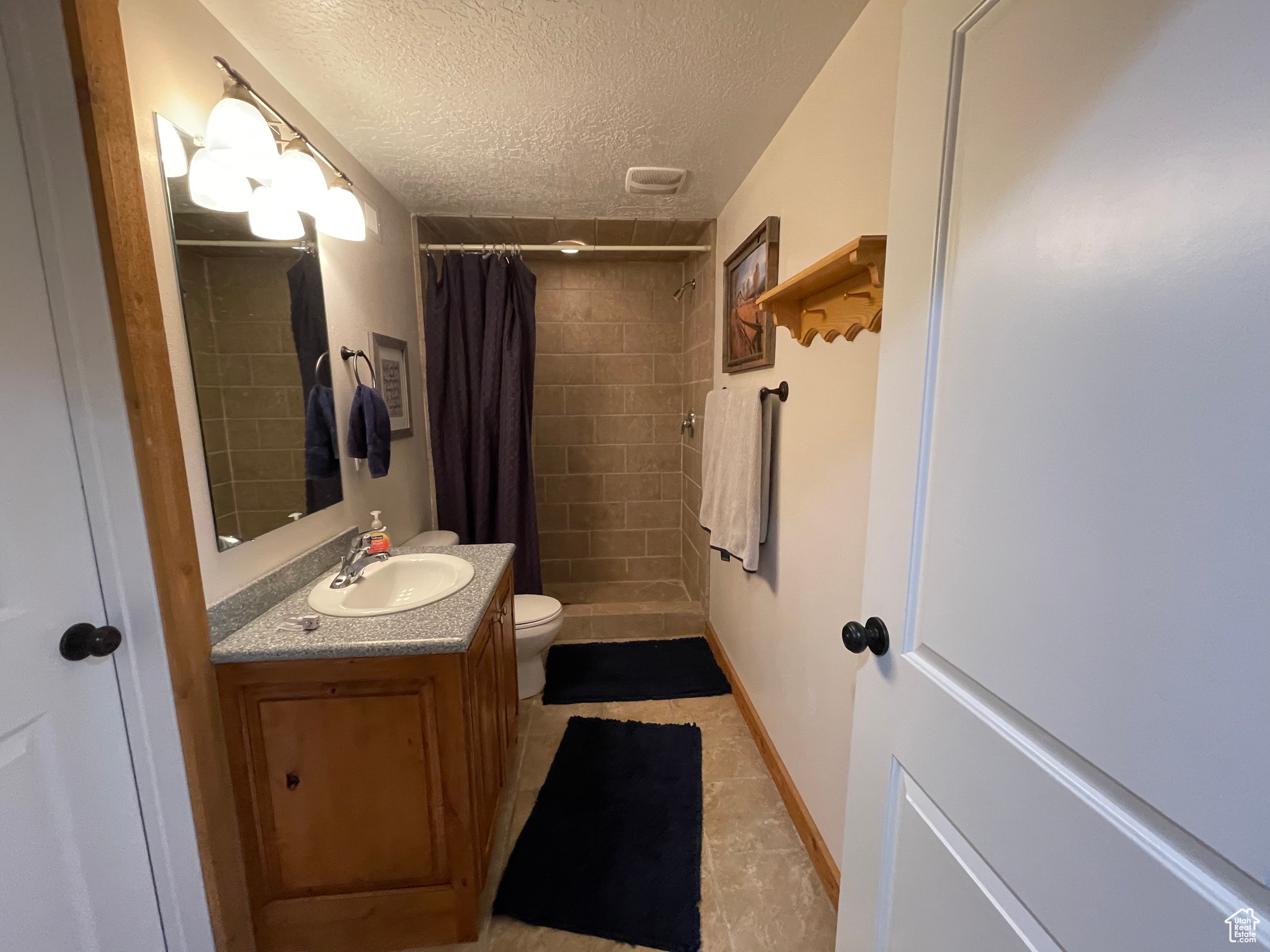 Bathroom featuring toilet, large vanity, a shower with shower curtain, tile flooring, and a textured ceiling