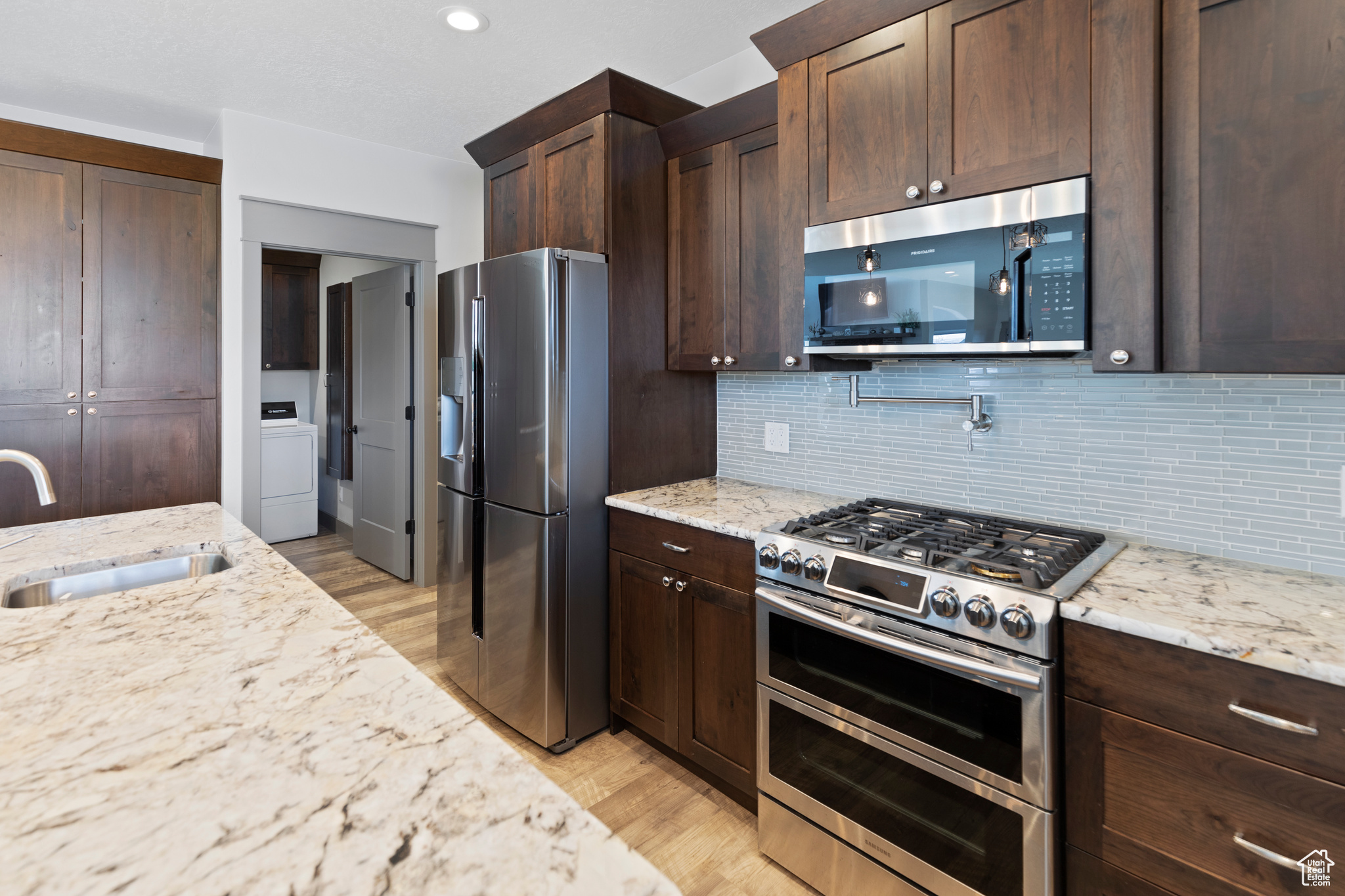 Kitchen with light hardwood / wood-style floors, appliances with stainless steel finishes, light granite counters, sink, and tasteful backsplash