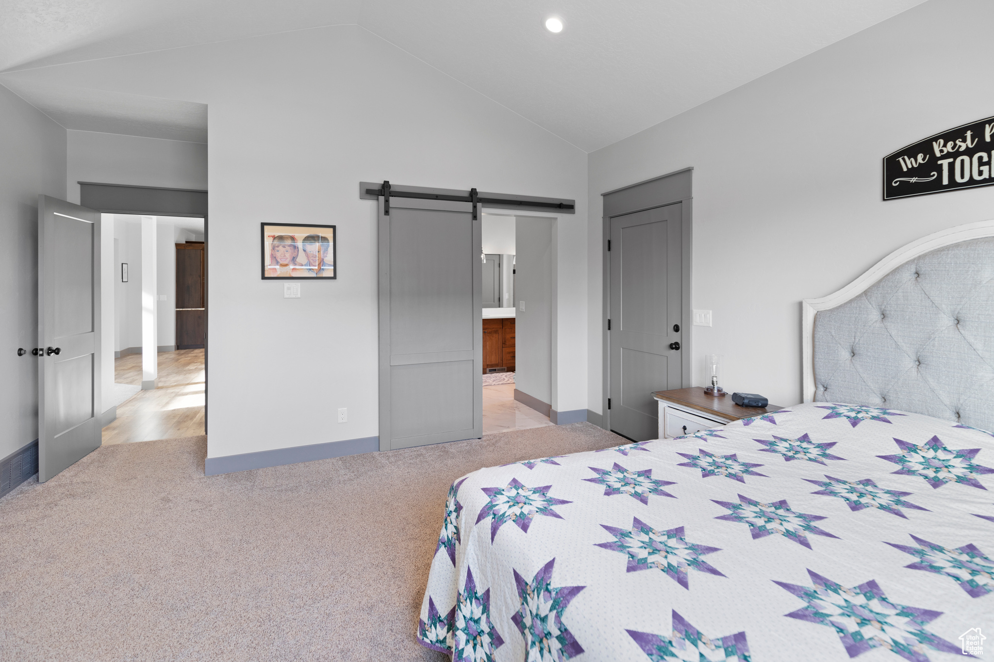 Master bedroom featuring connected bathroom, high vaulted ceiling, a barn door, and light carpet floors