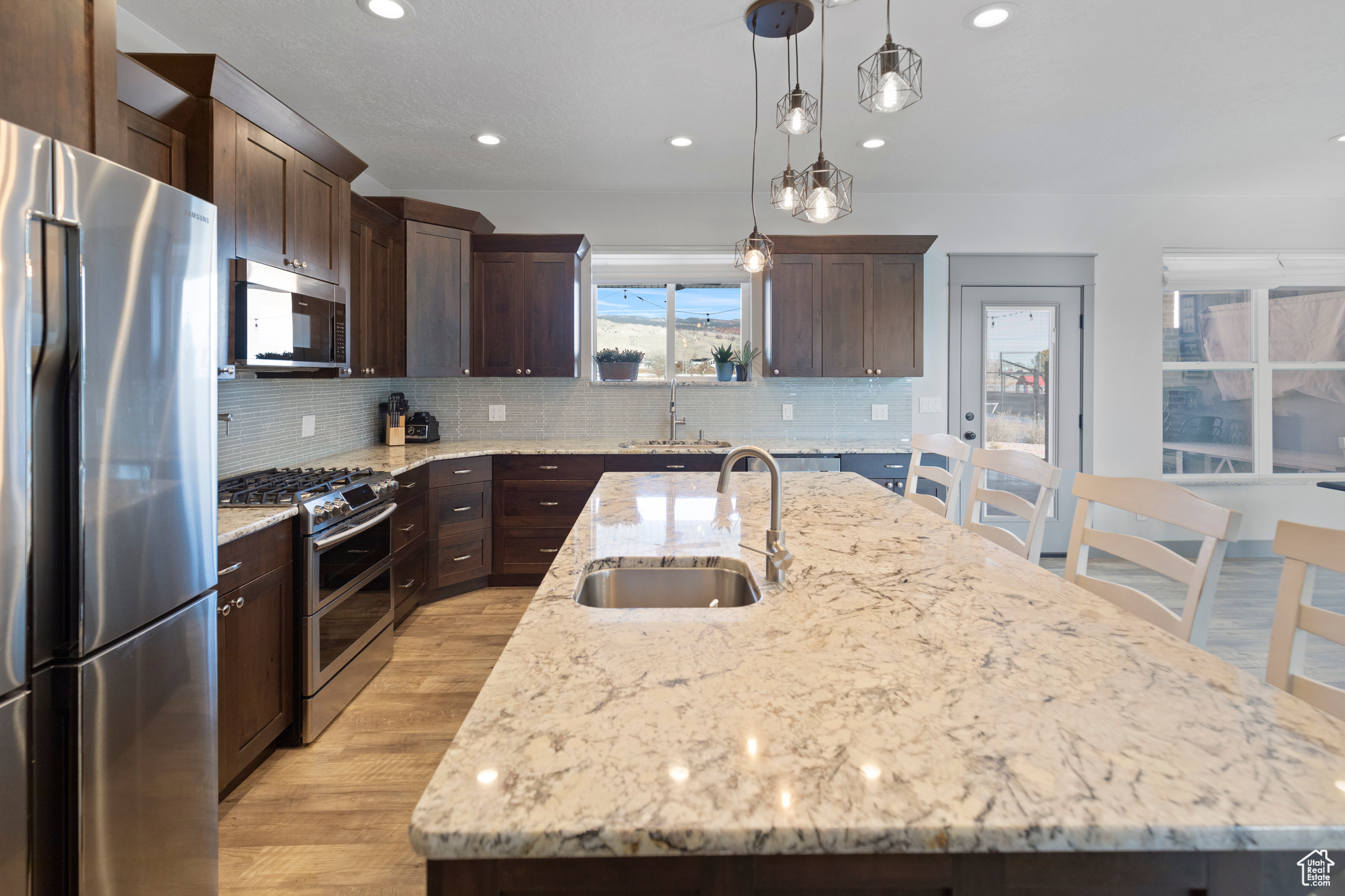 Kitchen with sink, appliances with stainless steel finishes, a kitchen island with sink, and hanging light fixtures