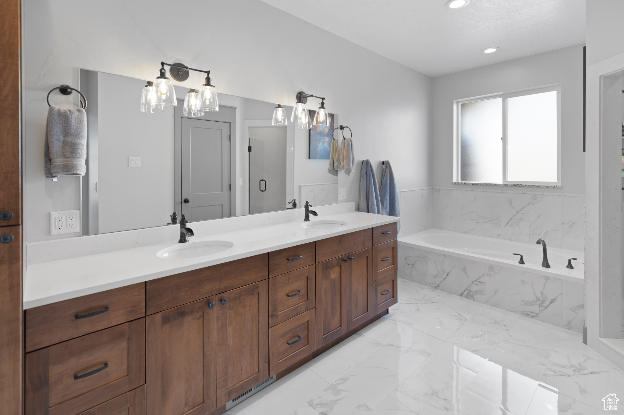 Bathroom with tile floors, a notable chandelier, tiled bath, and dual vanity