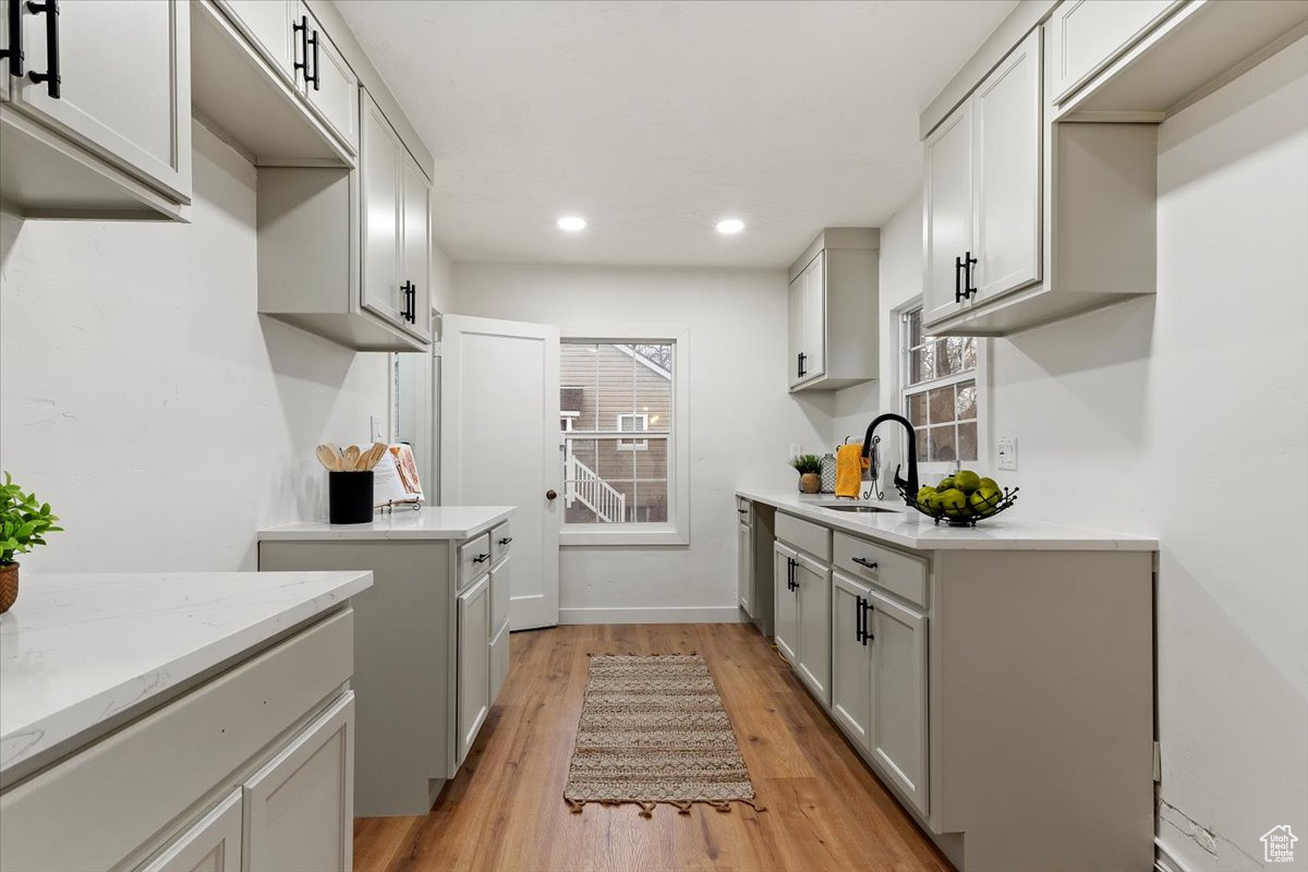 Kitchen featuring light hardwood / wood-style floors, sink, light stone counters, and gray cabinets